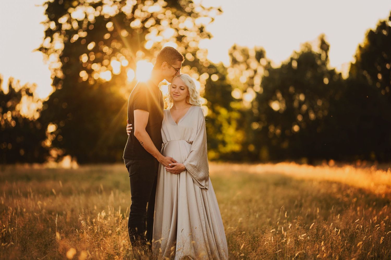 Couple embracing in golden sunset light in a meadow, woman in elegant gown, romantic outdoor photography.