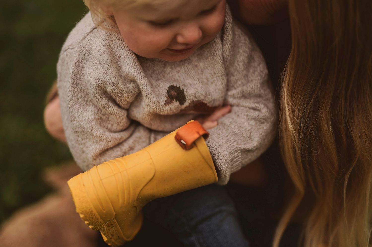 Close-up detail of yellow rain boots and grey sweater during an autumn outdoor session.