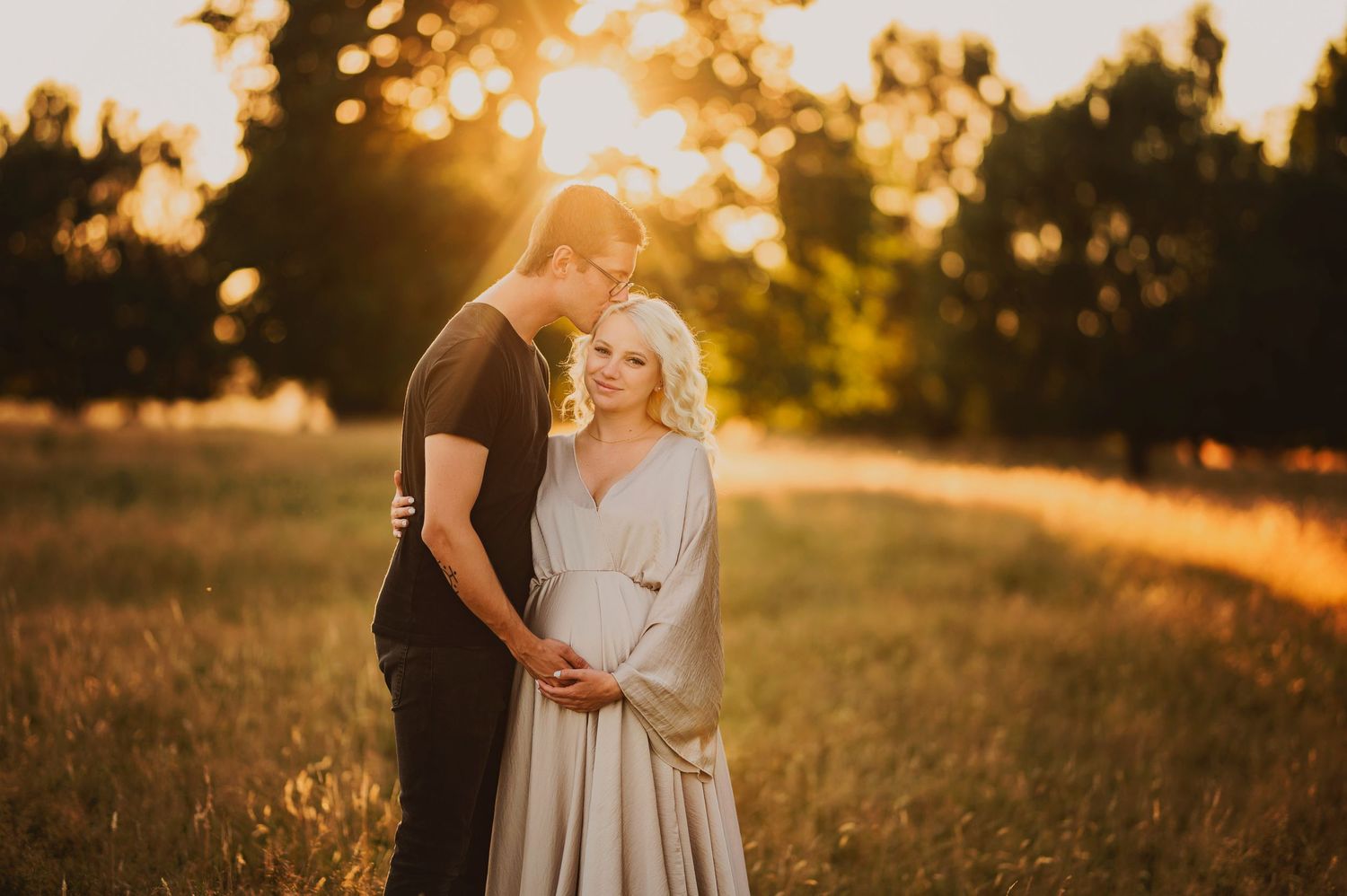 Intimate maternity photo with couple embracing in sunlit meadow at golden hour.