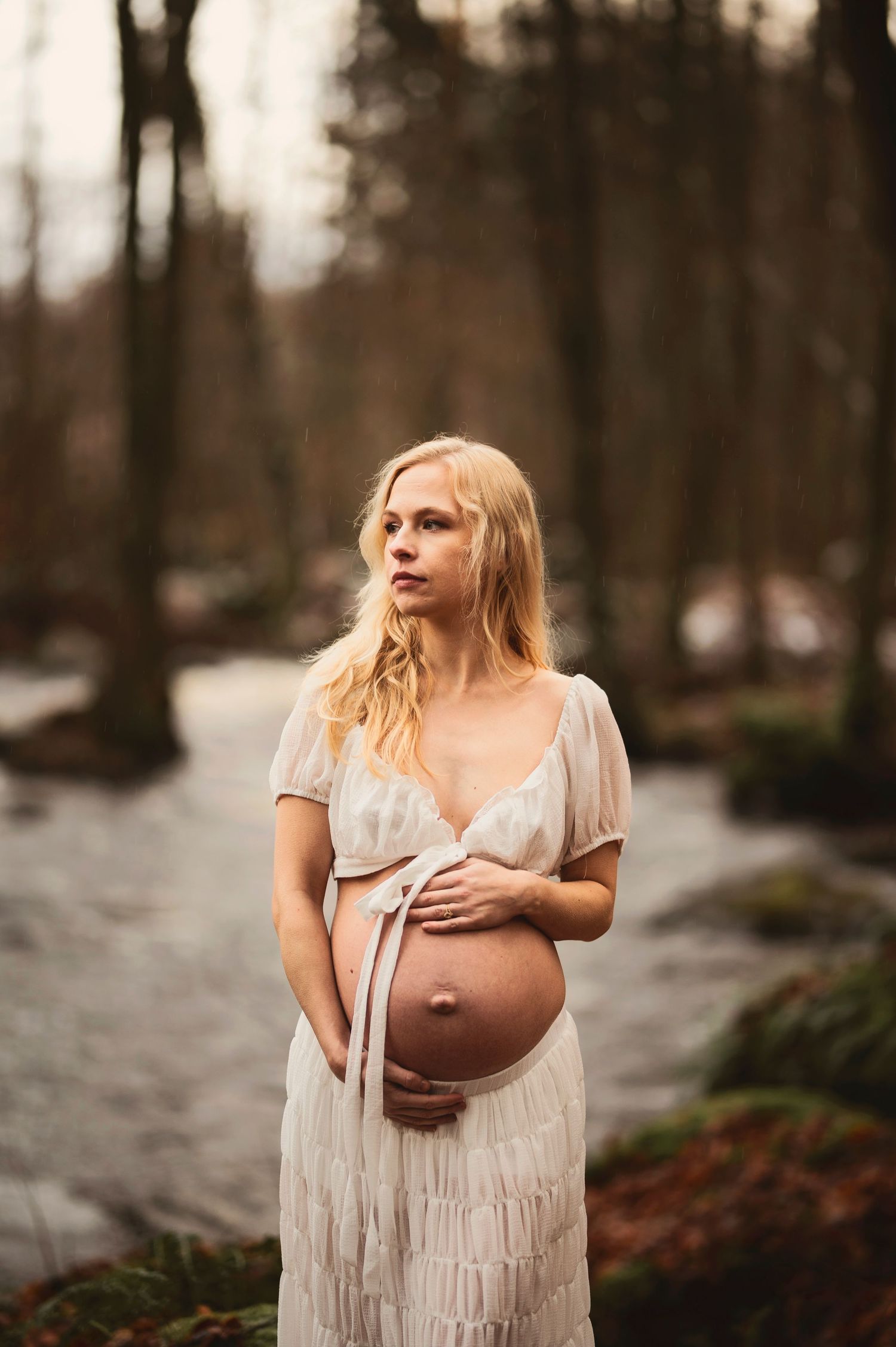 Vacker gravid kvinna på fotografering vid en bäck. Fotograf är Lovestories By Sara.