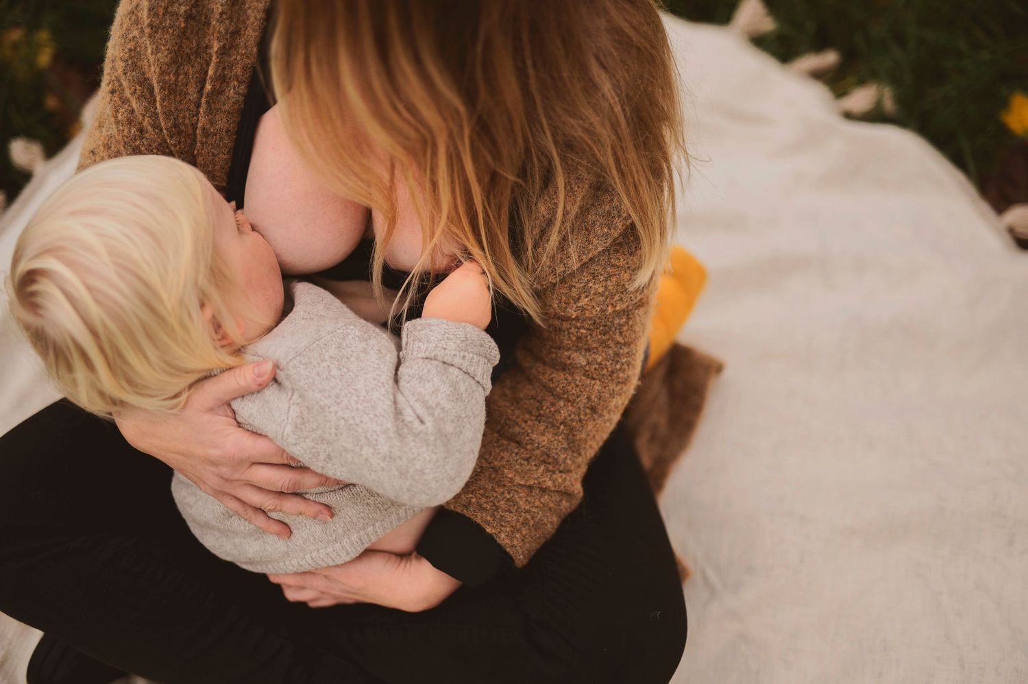 Intimate nursing moment captured from above on white blanket outdoors.