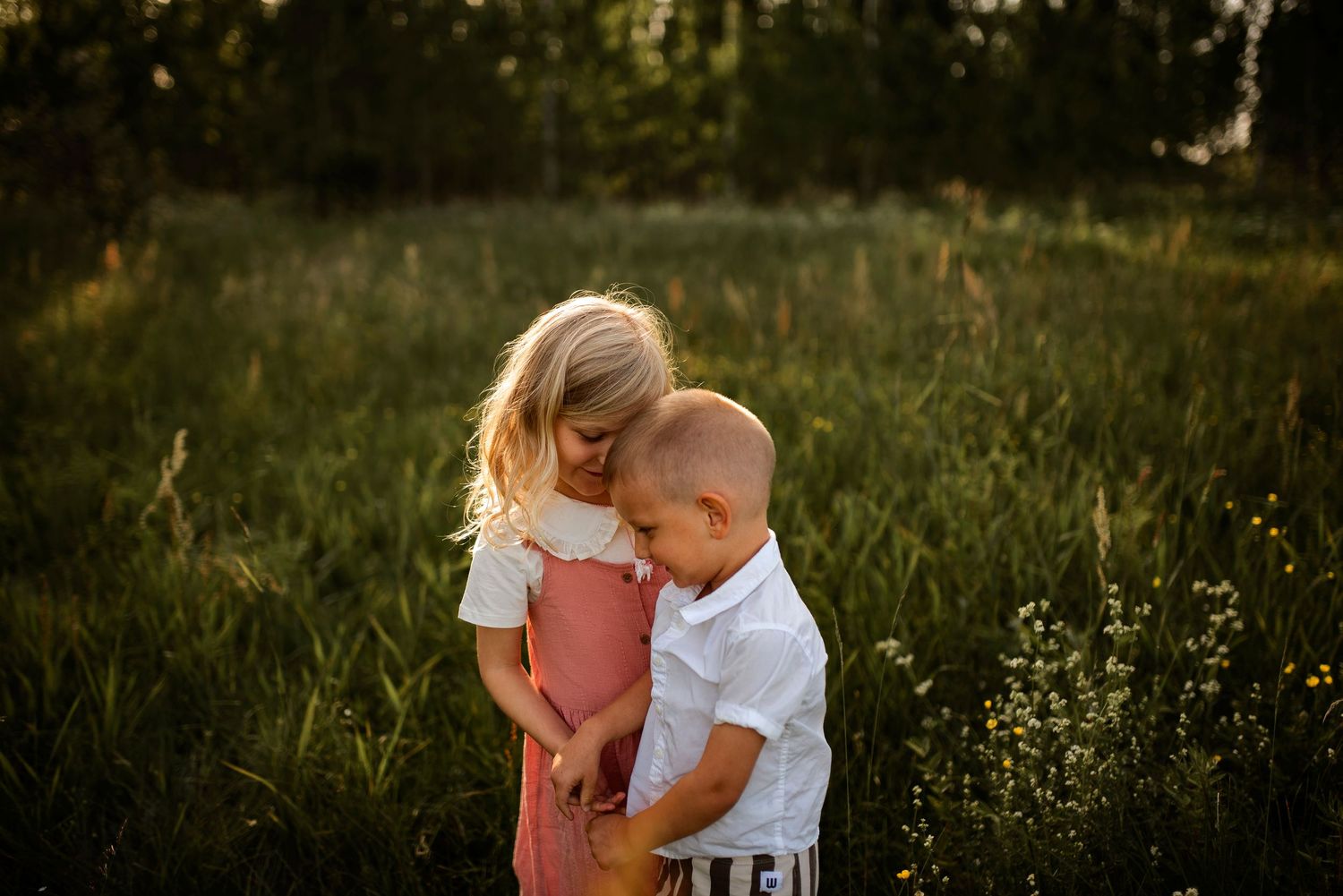 Two children sharing a quiet moment in sunlit field with wildflowers.