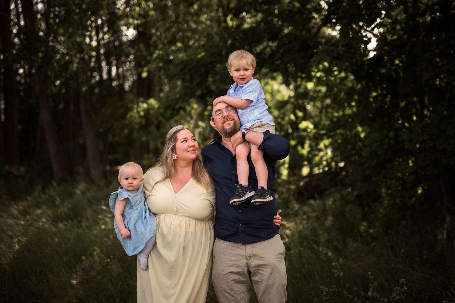 A family photo in a forest setting wearing coordinated cream and blue outfits at sunset.