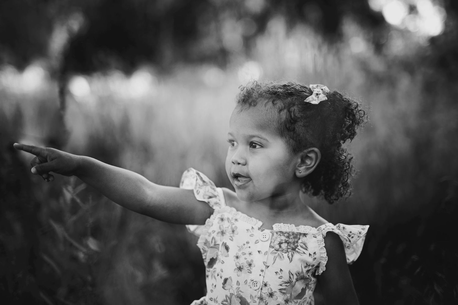 A child in a floral dress points excitedly while standing in nature.