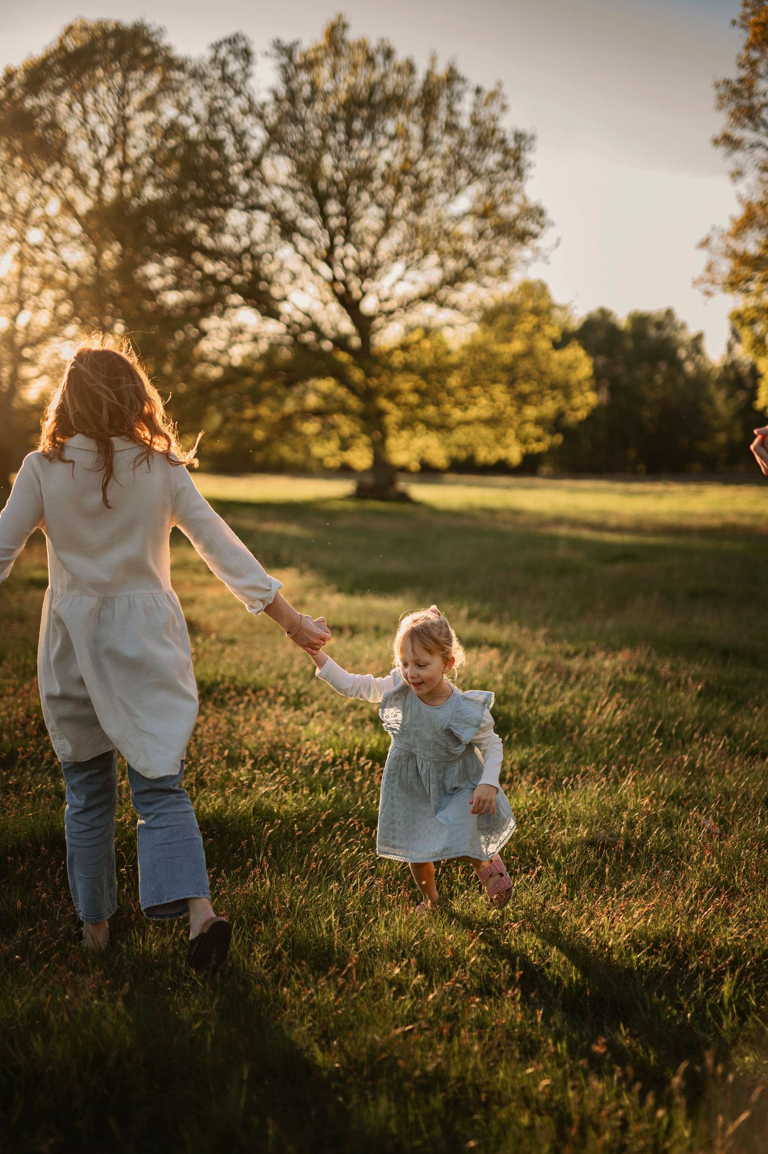 Parent and child holding hands while running through sunlit field at sunset.