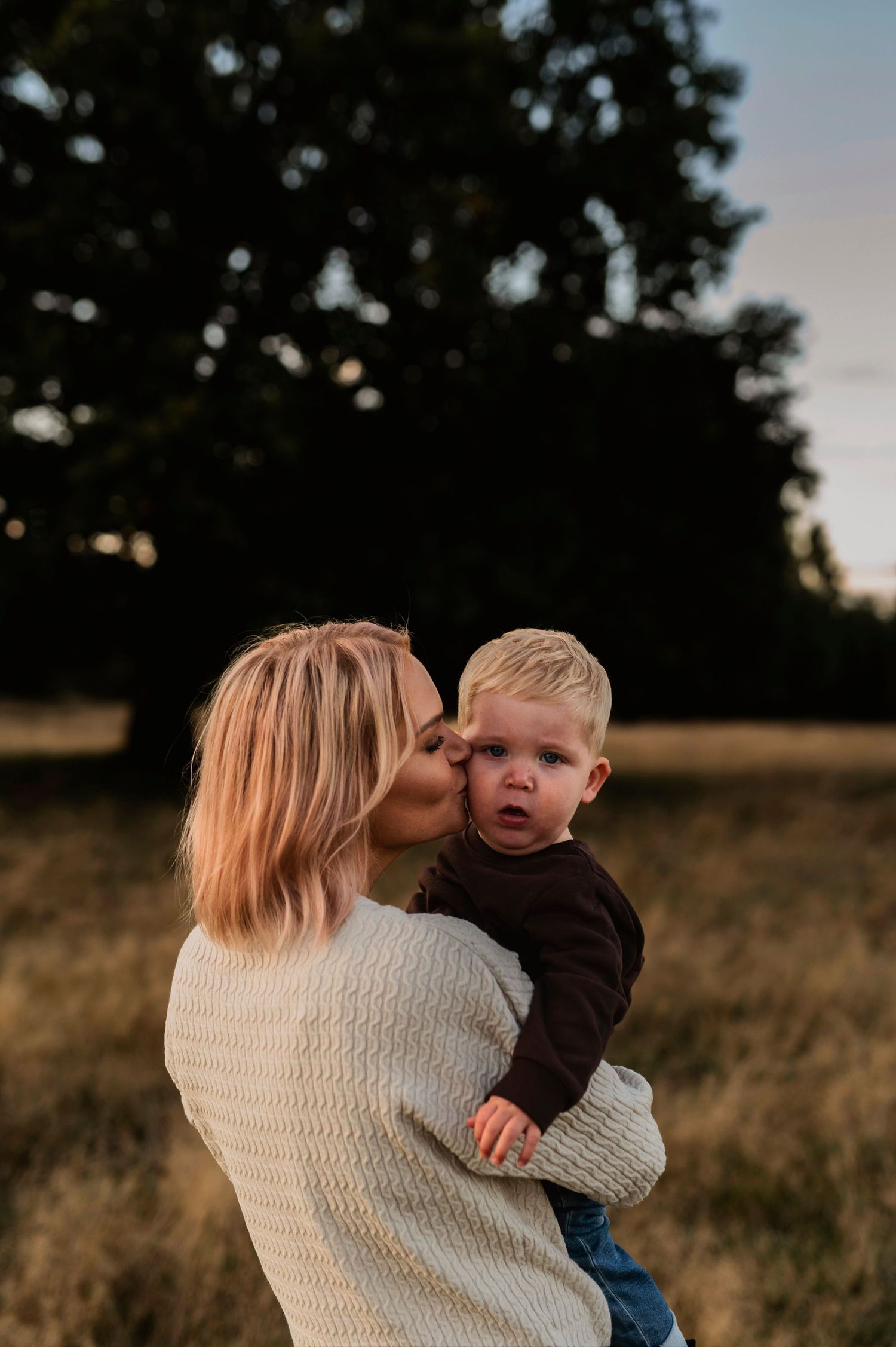 A tender moment between parent and child in a warm outdoor setting at dusk.