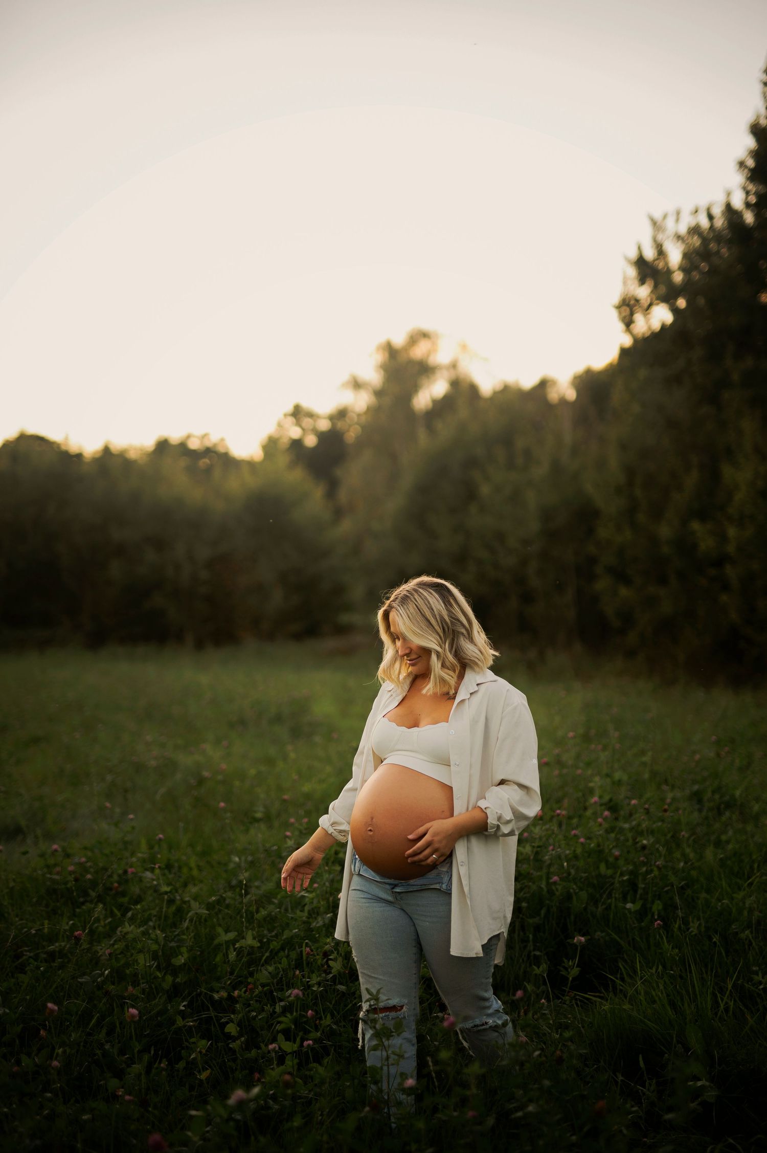 Natural maternity photograph in distressed jeans and white shirt at sunset.