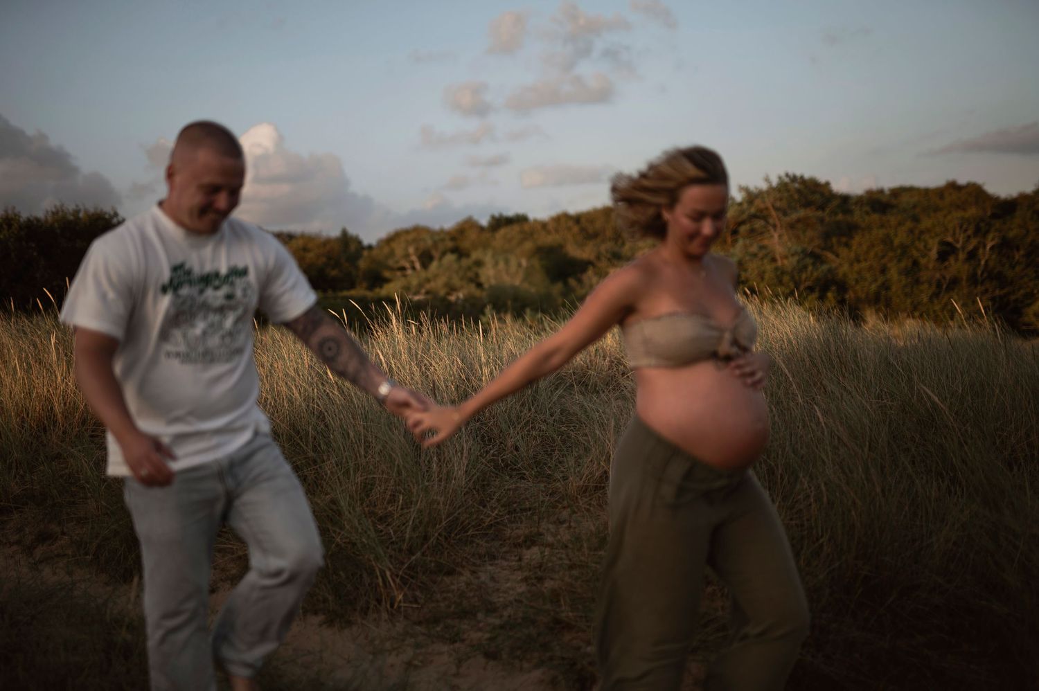 Pregnant couple playfully posing together in a golden field during sunset.