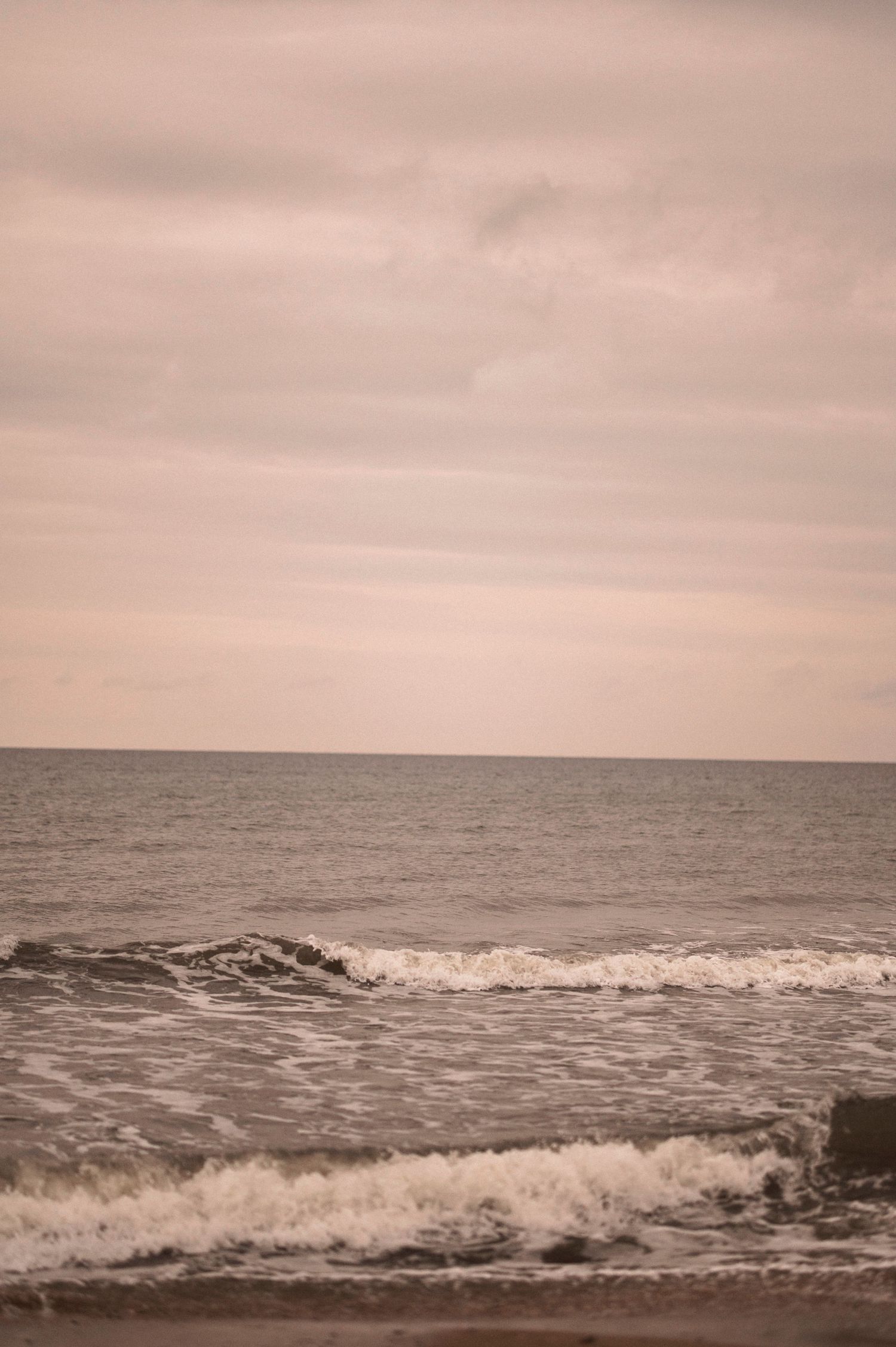 Ocean waves crash against the shore under a pink cloudy sunset sky.