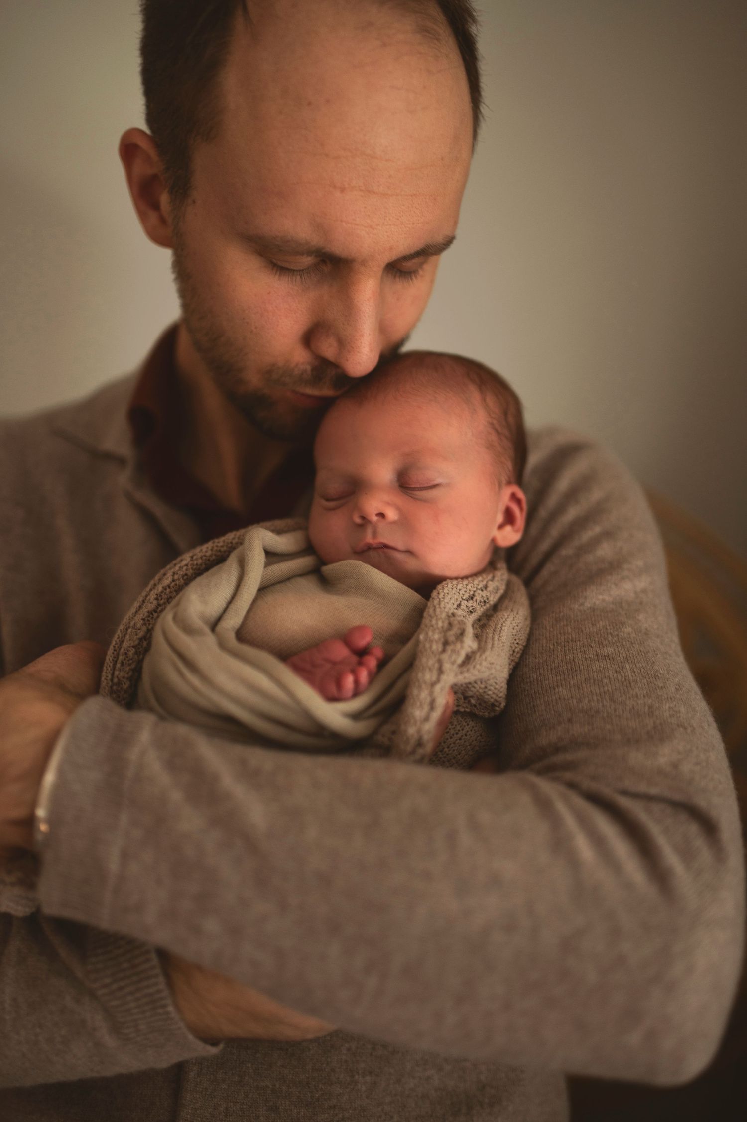 Tender moment between parent and sleeping newborn in soft lighting.