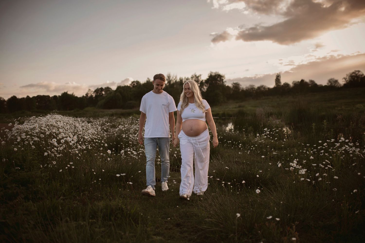 A romantic evening photoshoot in a field of daisies with soft golden sunset lighting.