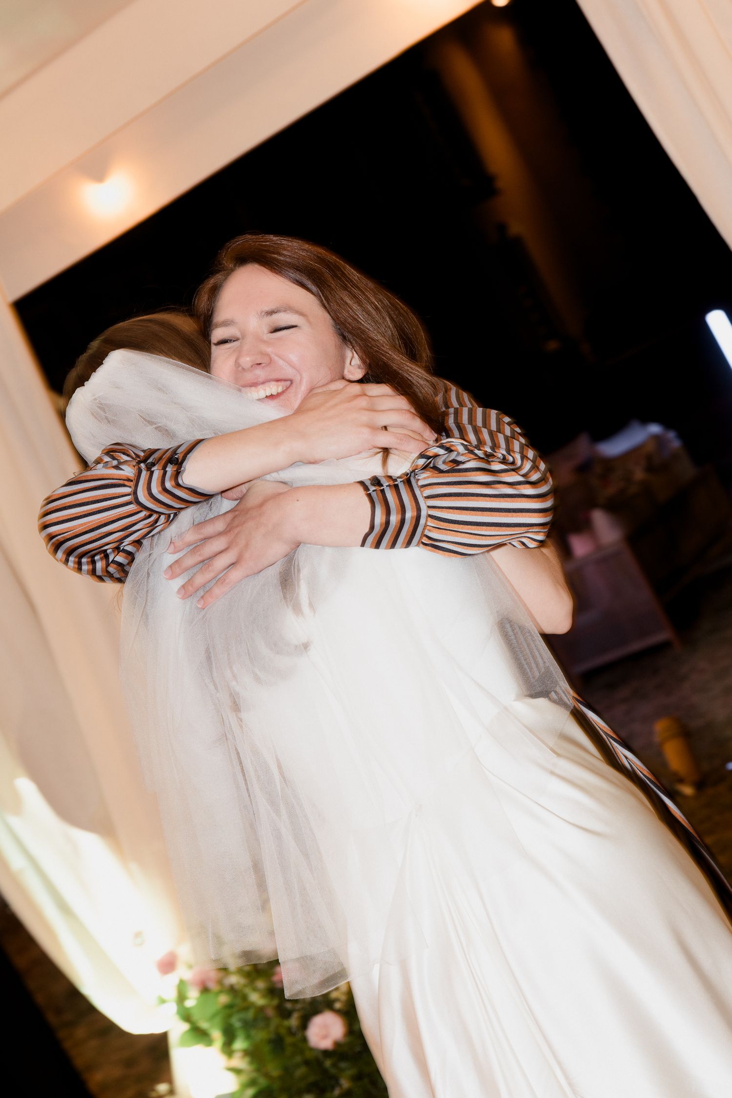 A couple embraces in a tender moment during a wedding celebration with white dress and striped sleeves visible.