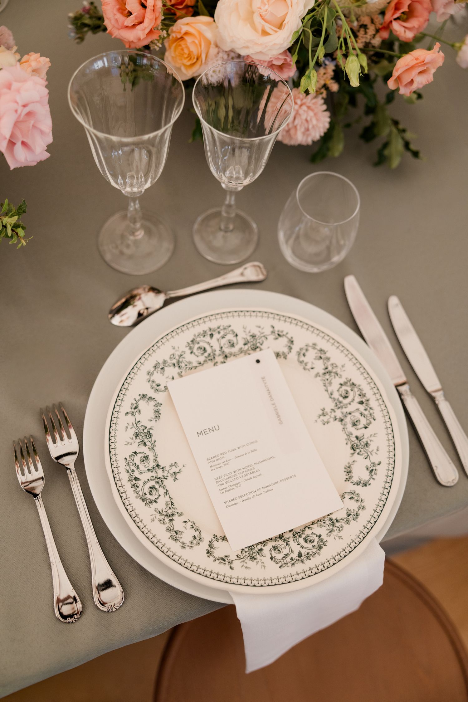 Elegant table setting with decorative floral plates, crystal glasses, and pink roses as centerpiece decorations.