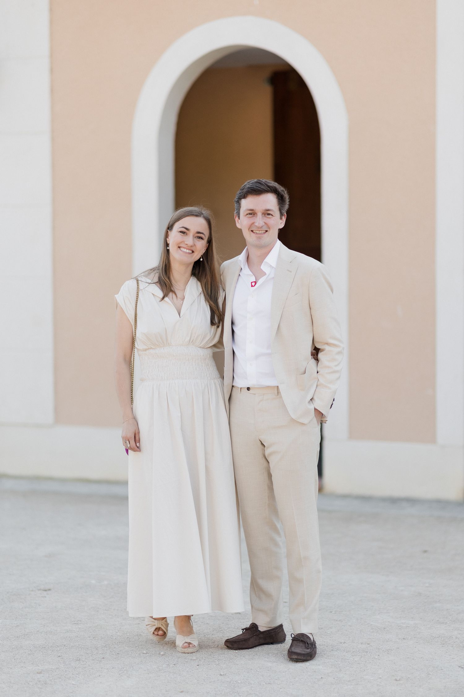 A couple in white and beige attire poses together against an arched Mediterranean-style building exterior. Loire valley wedding photographer