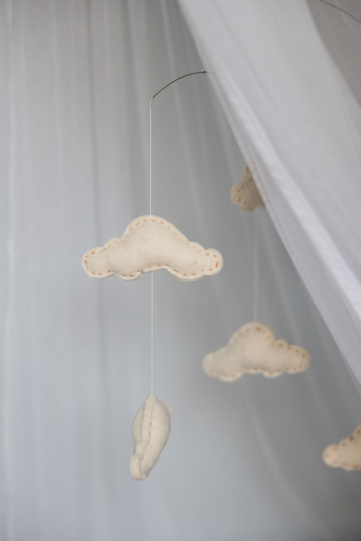 Handmade felt cloud baby mobile hanging from a white canopy in a soft, neutral nursery decor setting.