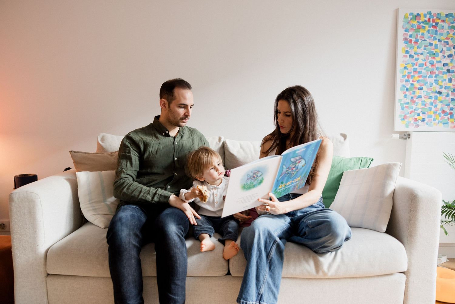 Family sitting on couch reading a colorful picture book together in a cozy living room.