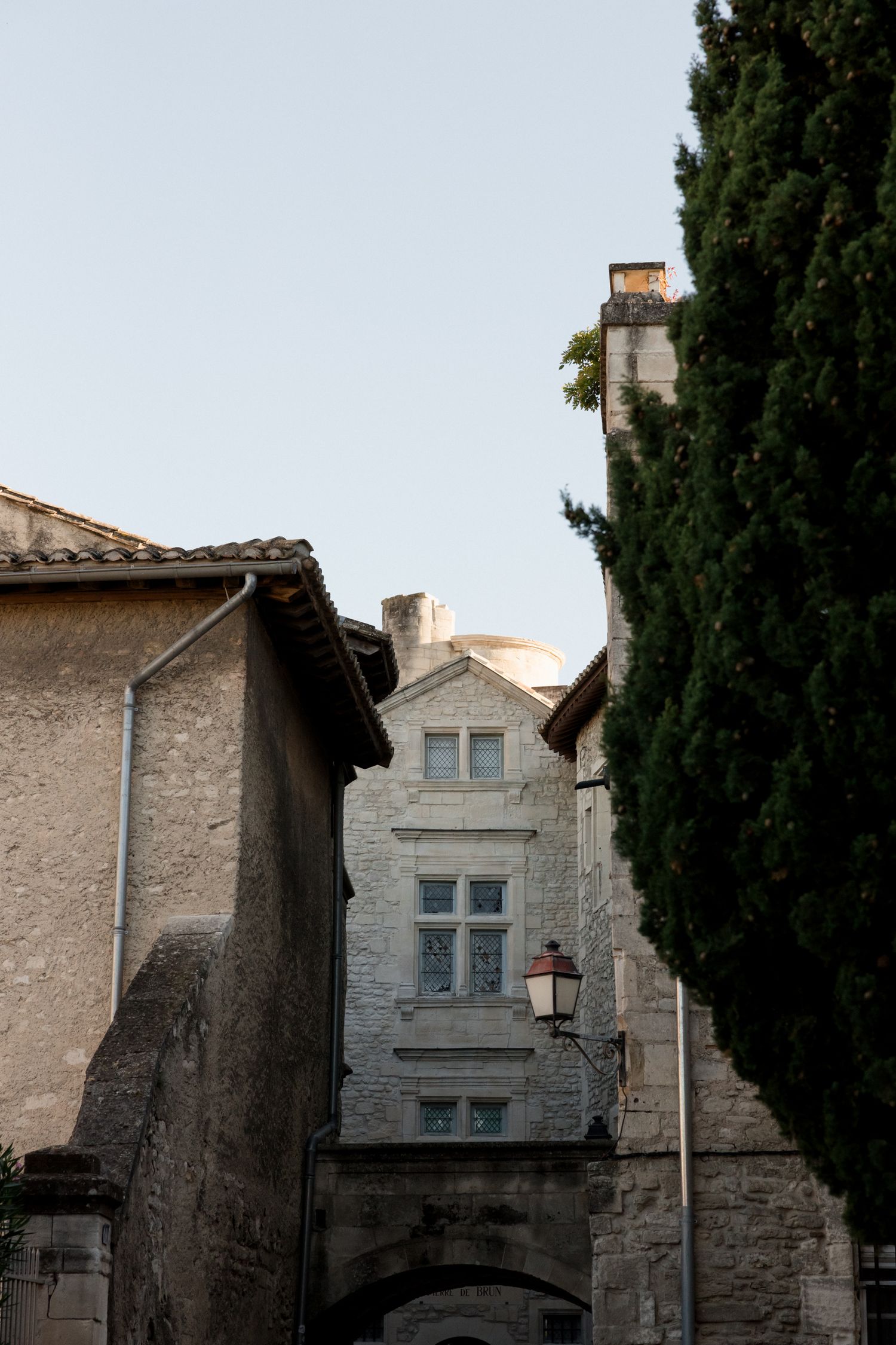 Ancient stone building with arched windows and cypress trees against a bright sky in a Mediterranean setting.