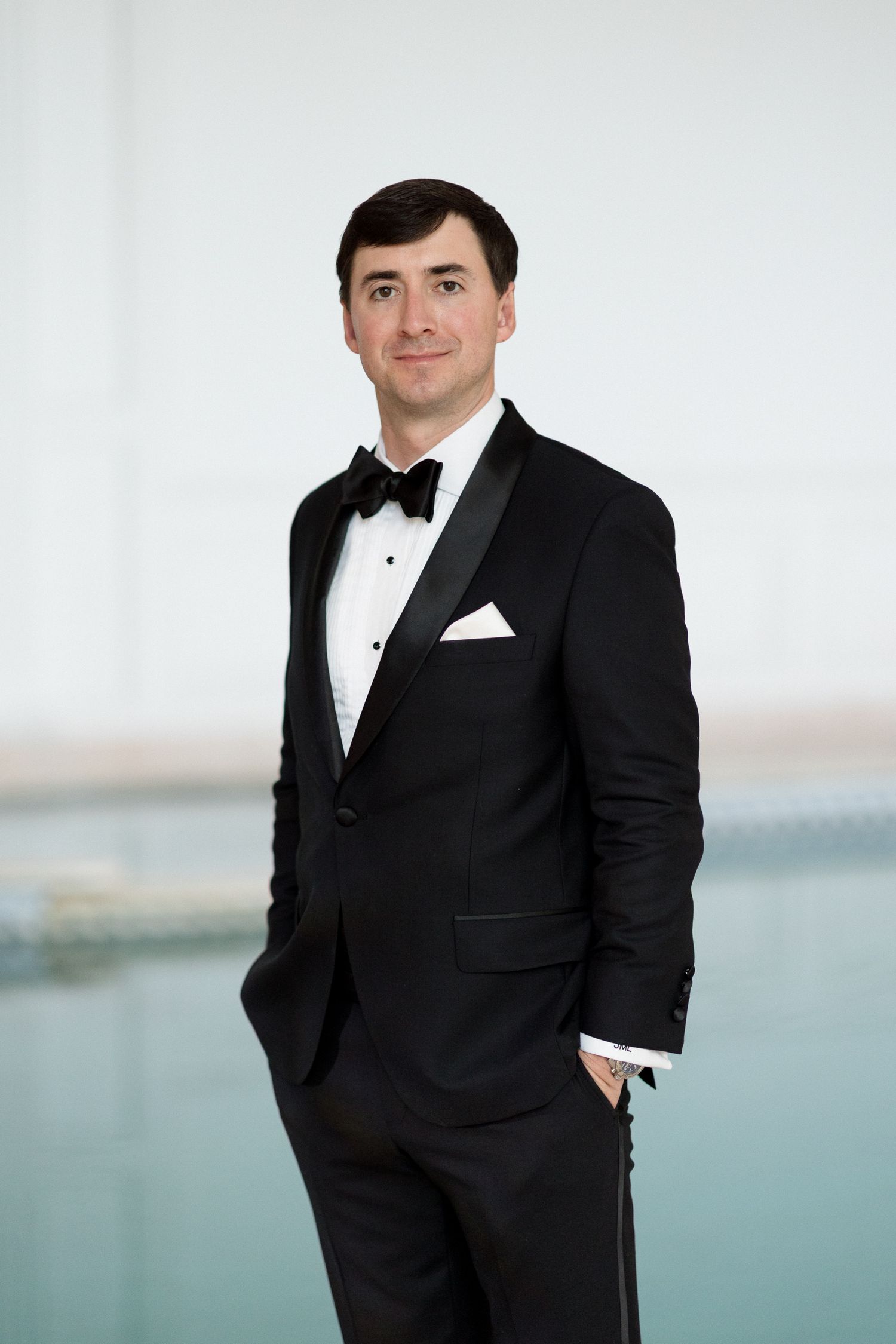 Professional portrait of someone in a classic black tuxedo with white dress shirt and bow tie against a light background. mariage grasse