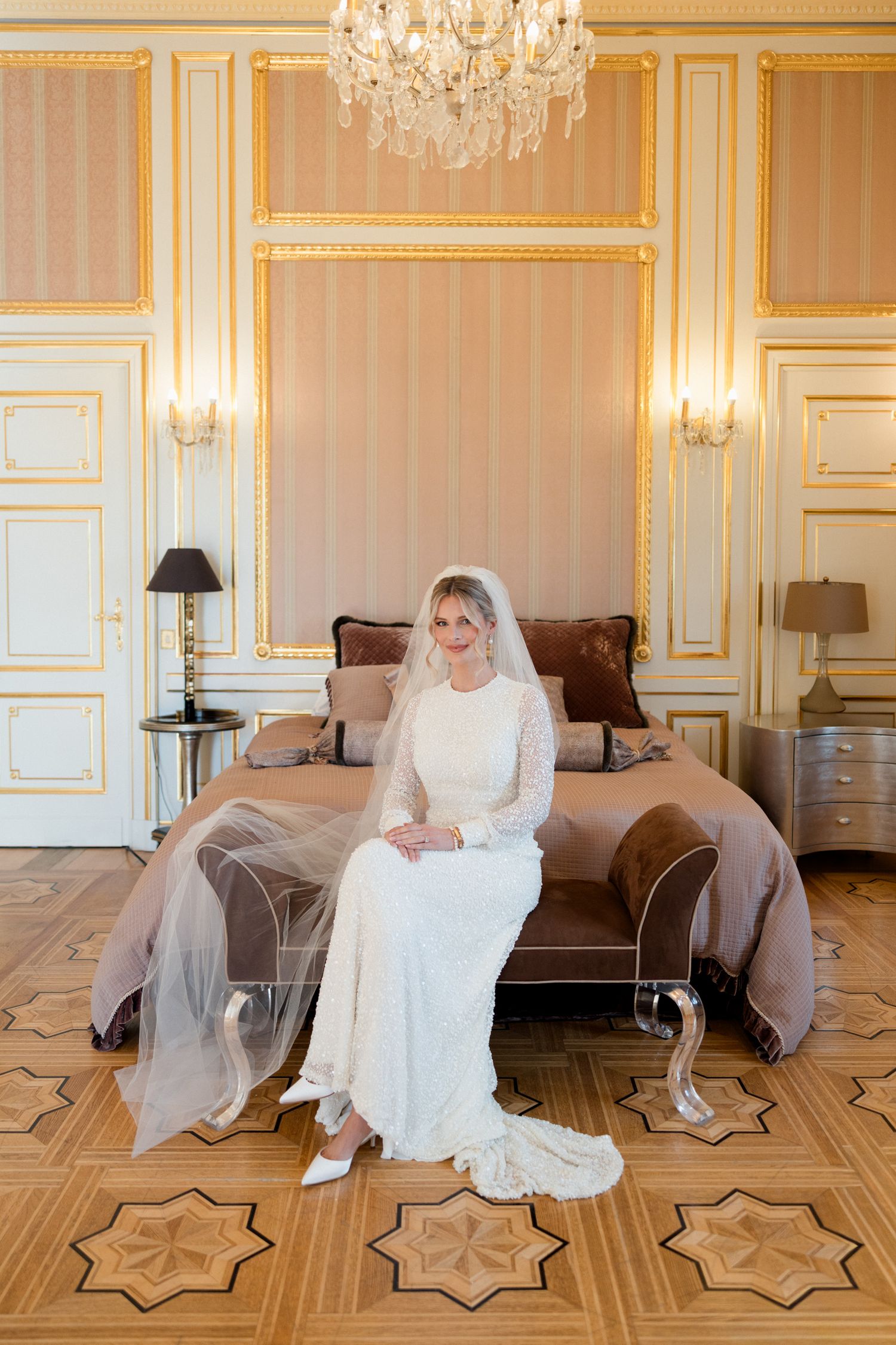 Elegant bridal scene in ornate room with crystal chandelier, gold trim walls and decorative parquet flooring.