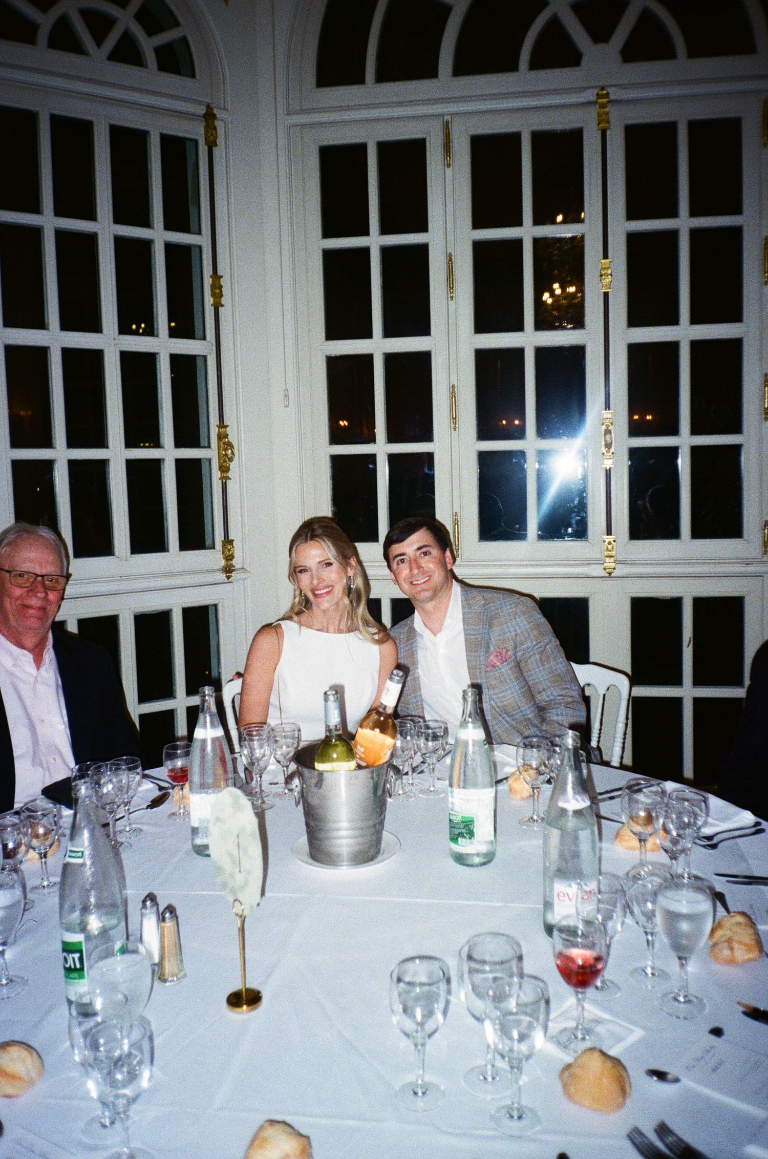 A panoramic view of an elegant dinner table set with white linens, glassware and guests seated in a formal dining room.