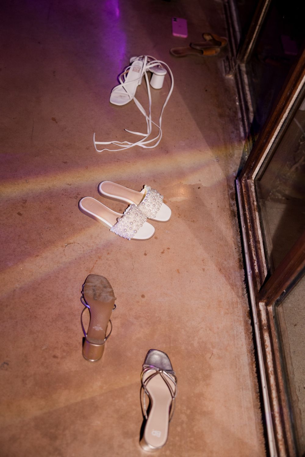 White sandals dance in stop motion sequence across a purple-lit hardwood floor creating a whimsical movement pattern.