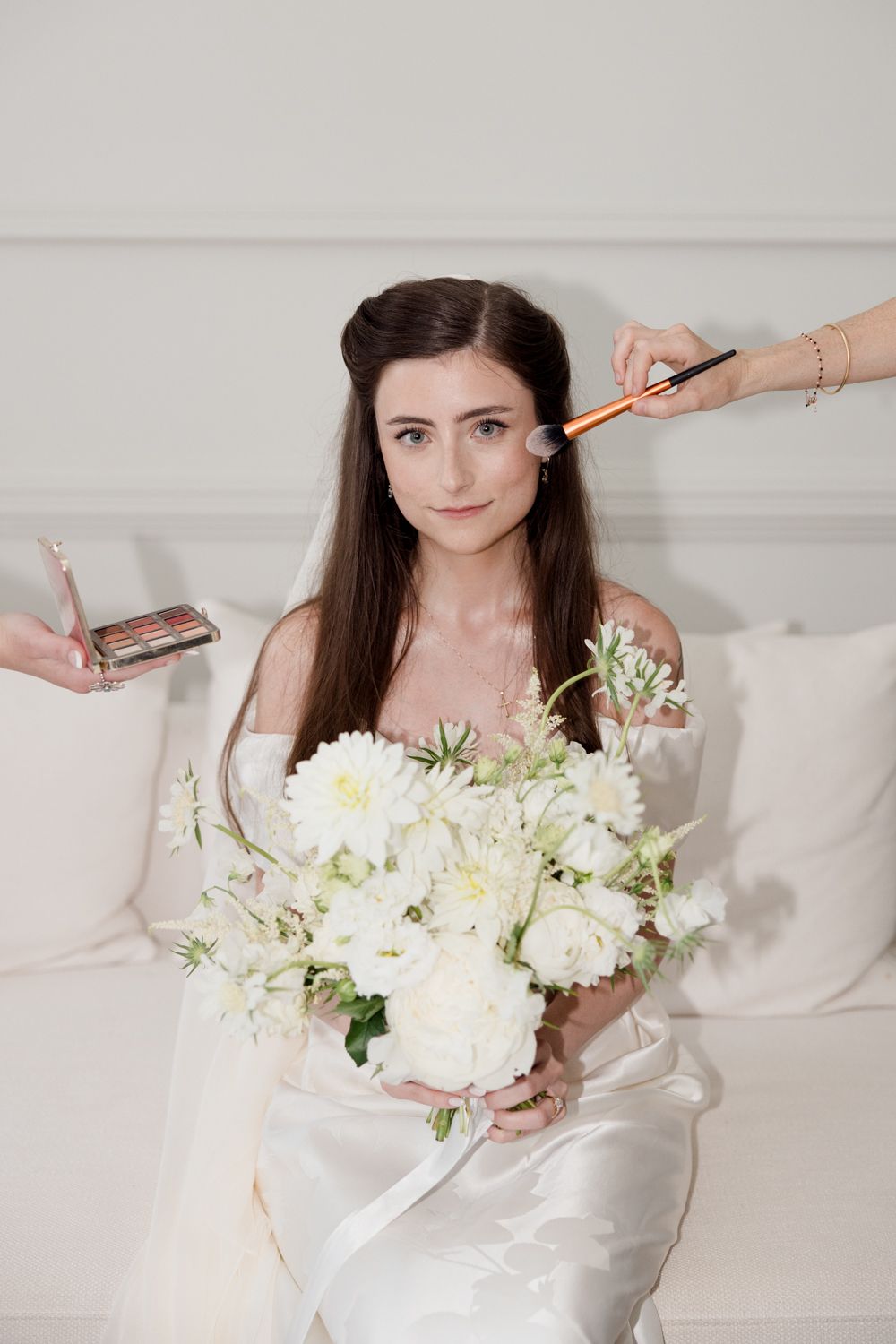 A figure wrapped in white bedding poses with a beautiful bouquet of fresh white flowers and greenery. Photographe mariage Provence
