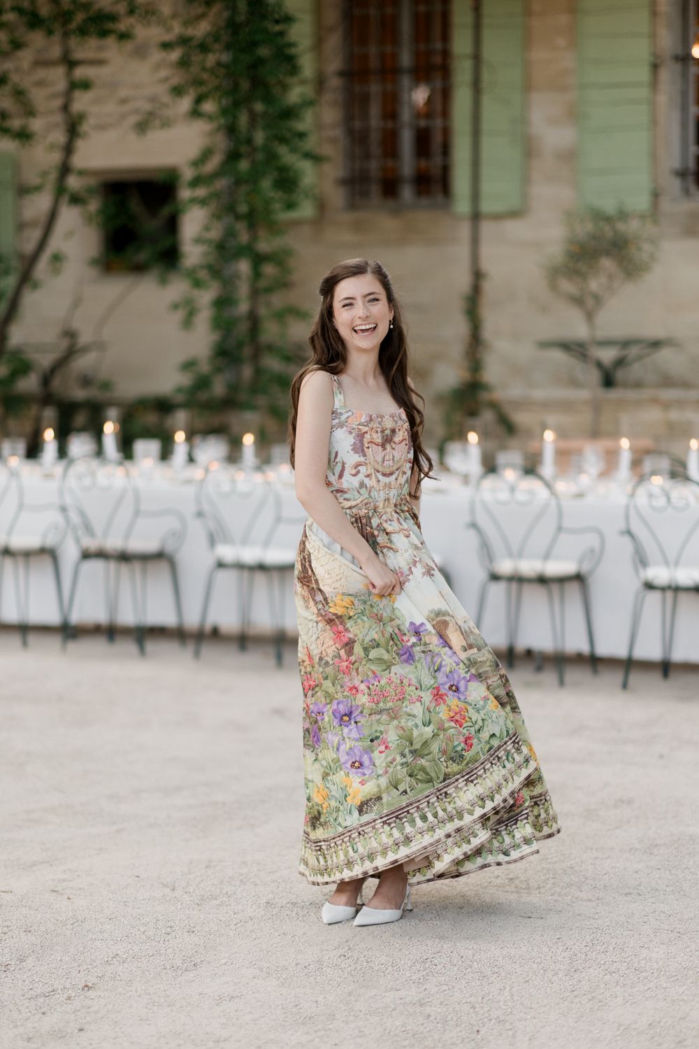 A floral dress swirls gracefully in an outdoor courtyard with white chairs arranged for an elegant event.