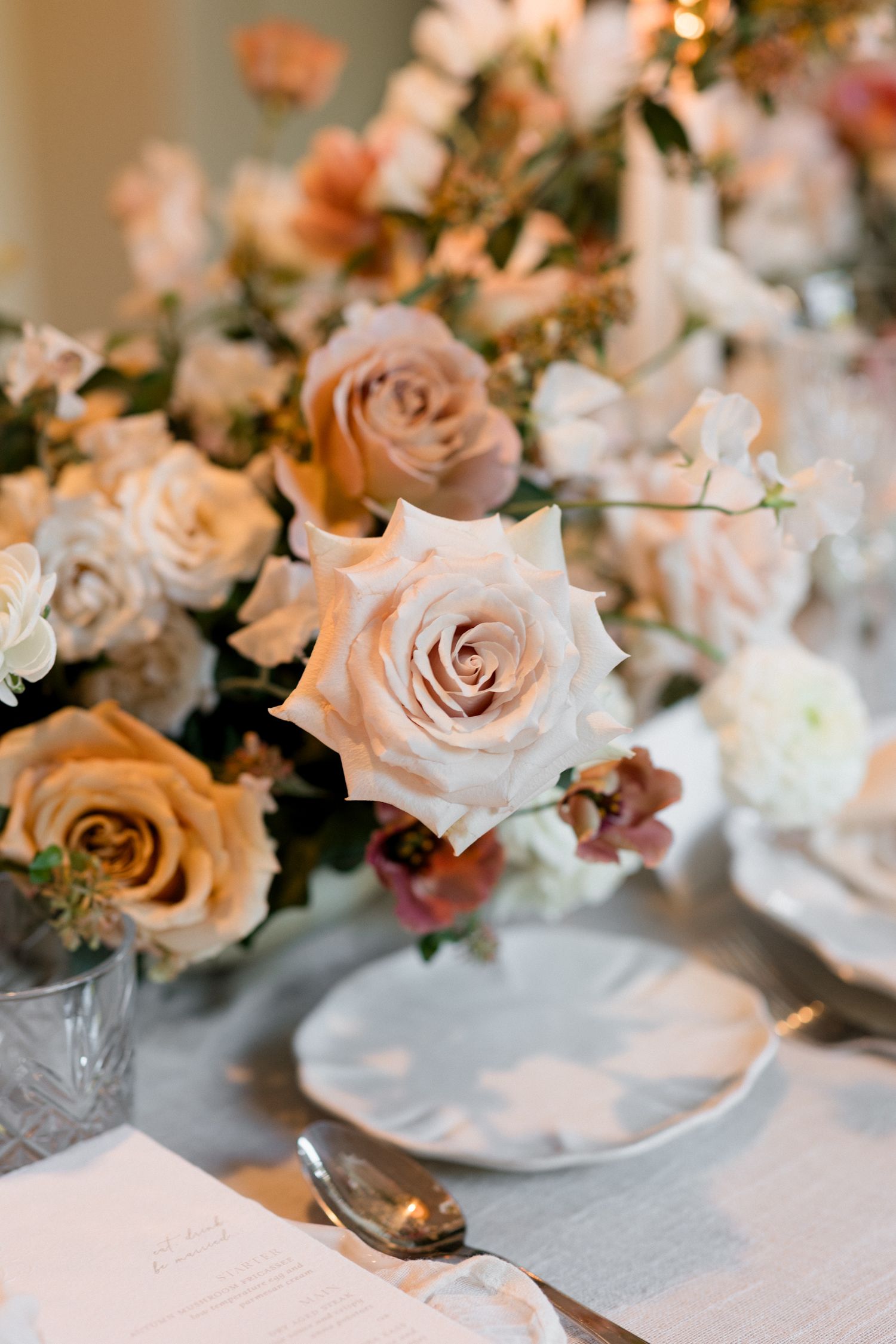 Elegant blush pink roses and white floral arrangements in crystal vases create a romantic wedding table centerpiece.