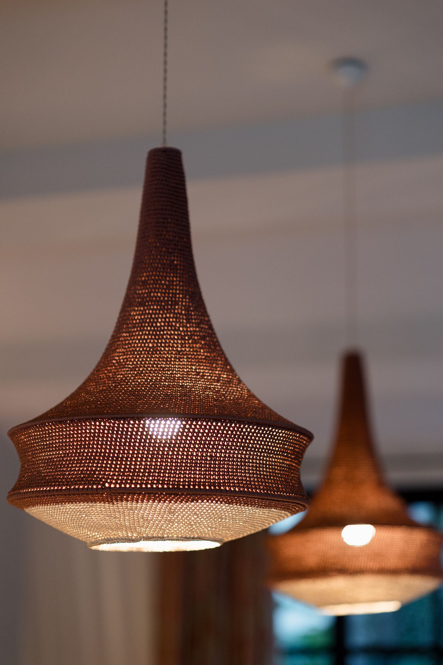 Modern copper mesh pendant lights with conical shapes hang from the ceiling creating warm ambient lighting in an interior space.