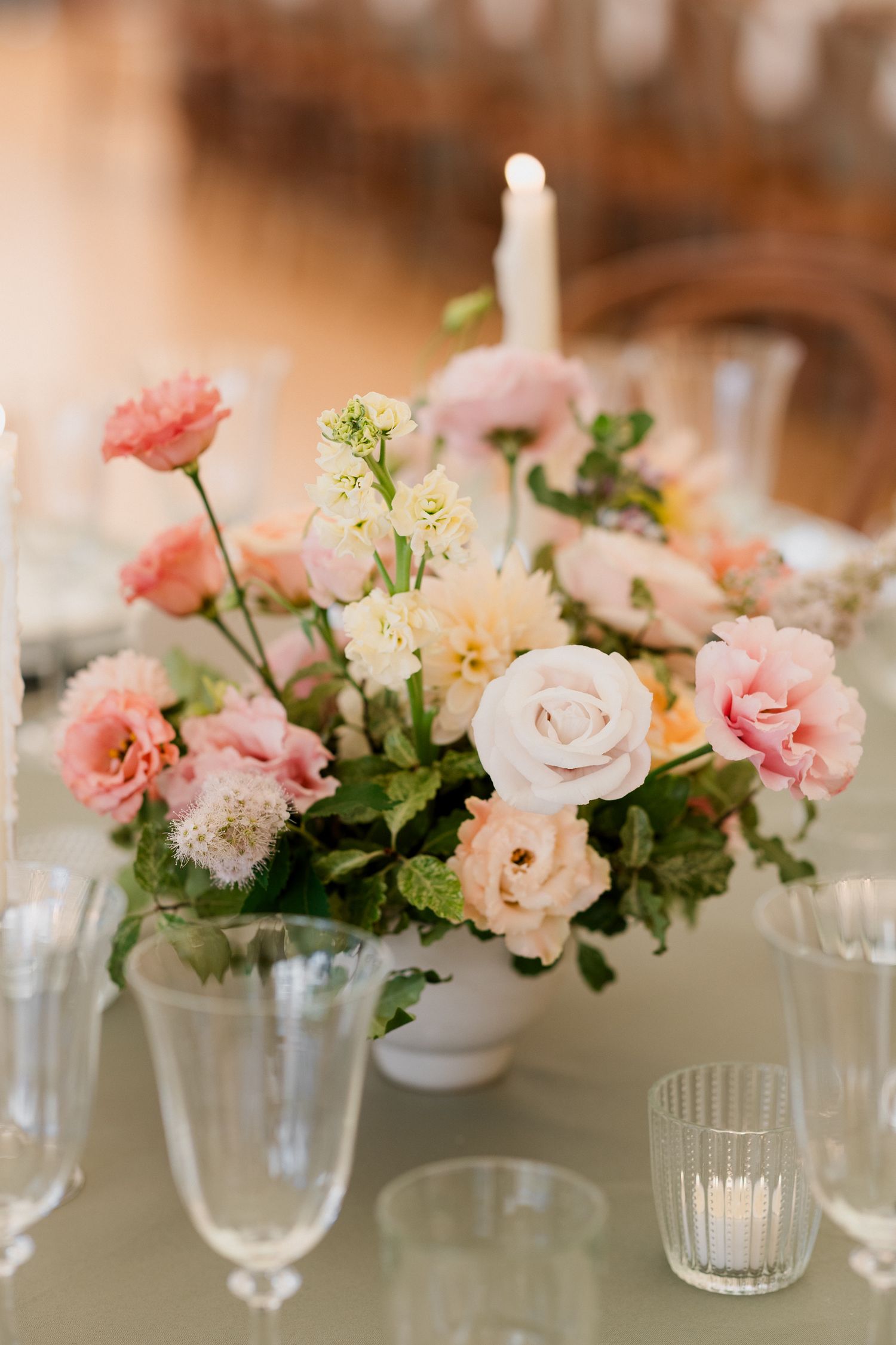 Elegant floral centerpieces with pink and white roses in glass vases create a romantic wedding table setting.