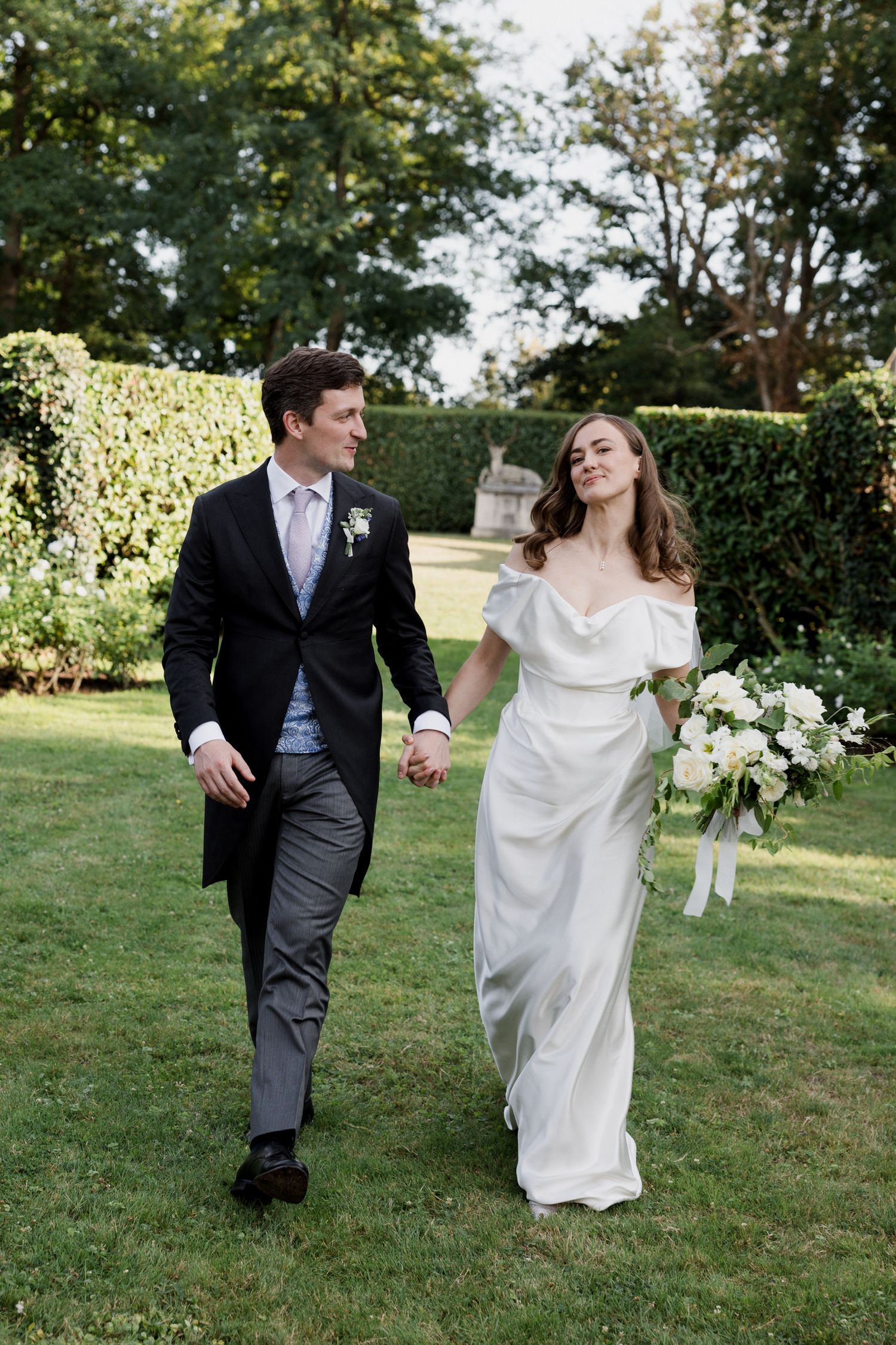 A newlywed couple walks joyfully together on a grassy lawn during their outdoor wedding photoshoot. Luxury wedding france