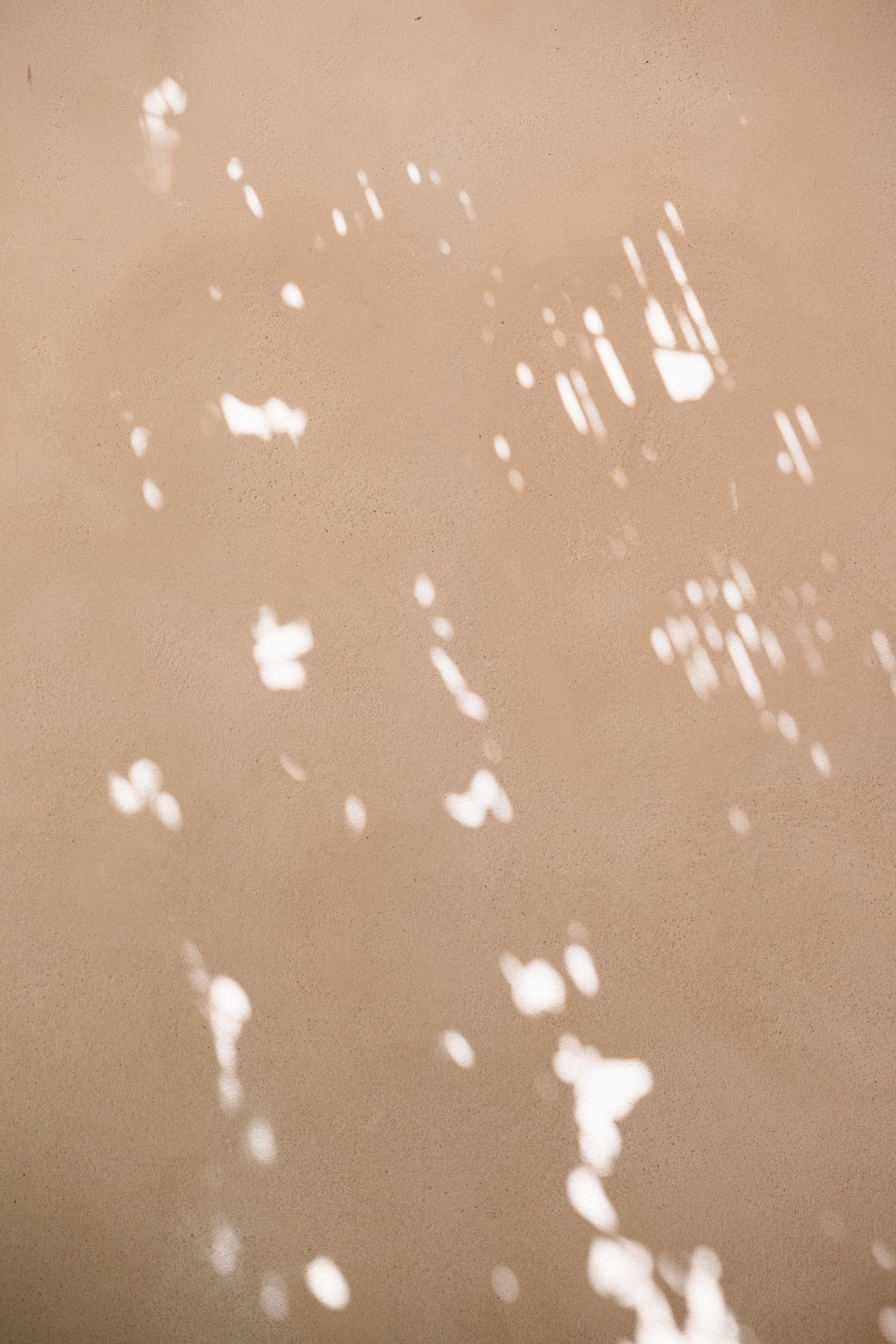A sepia-toned abstract pattern with scattered white spots and dots creating a speckled effect on a beige background.