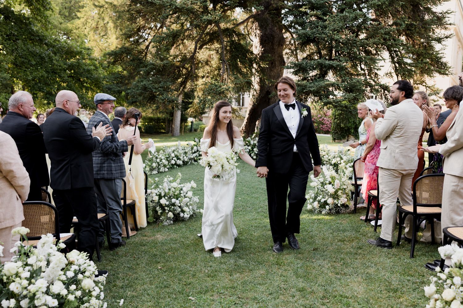 Wedding guests mingling on a lawn surrounded by mature trees during an outdoor celebration. Château des 3 Fontaines wedding Provence