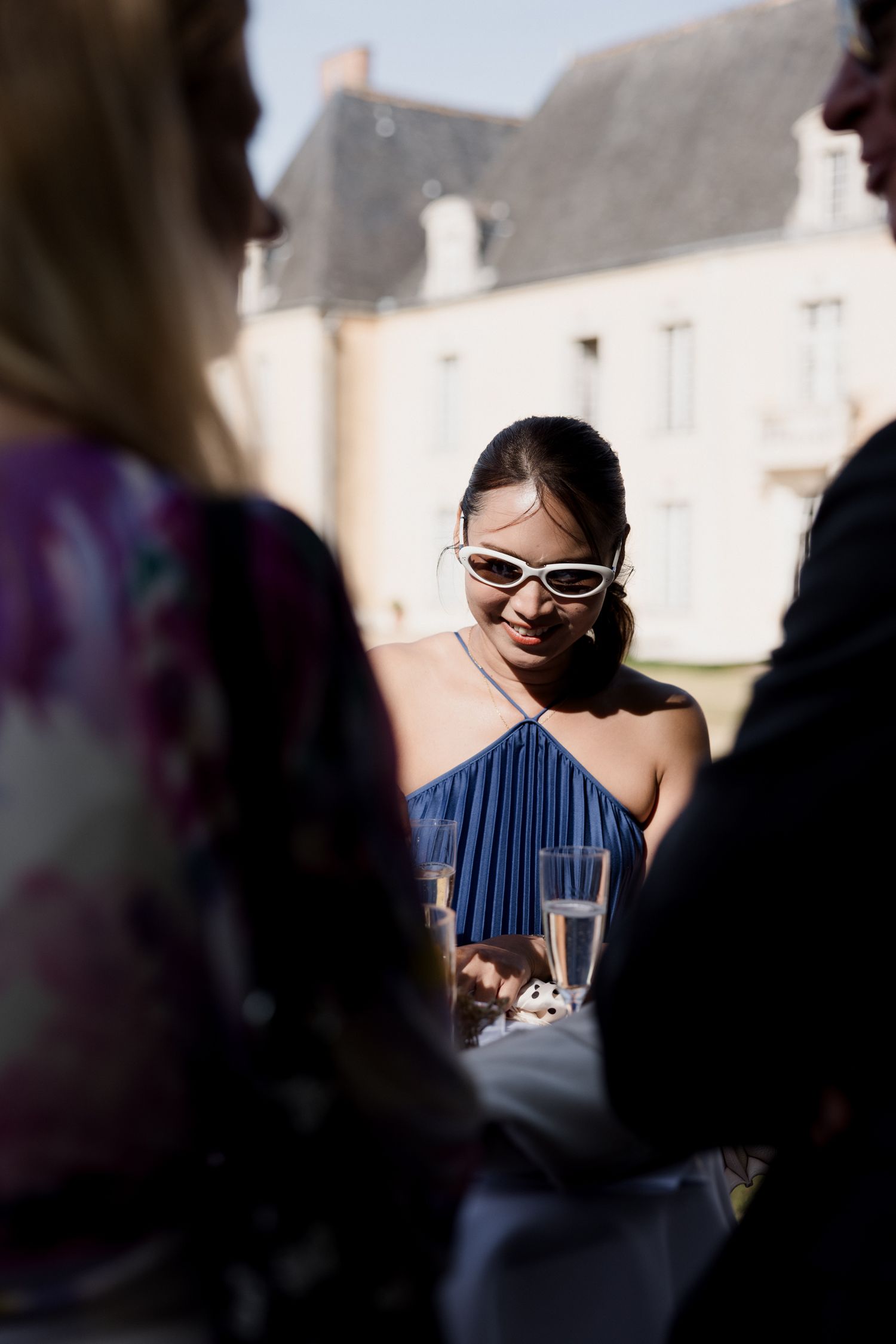 A person in sunglasses and a blue striped dress smiles during an outdoor gathering.