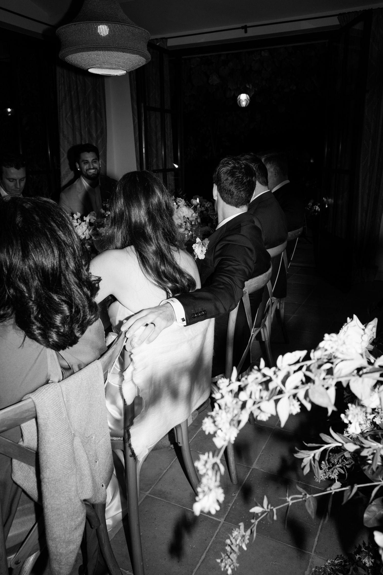 Black and white photo of a dimly lit indoor celebration with decorative white flowers.