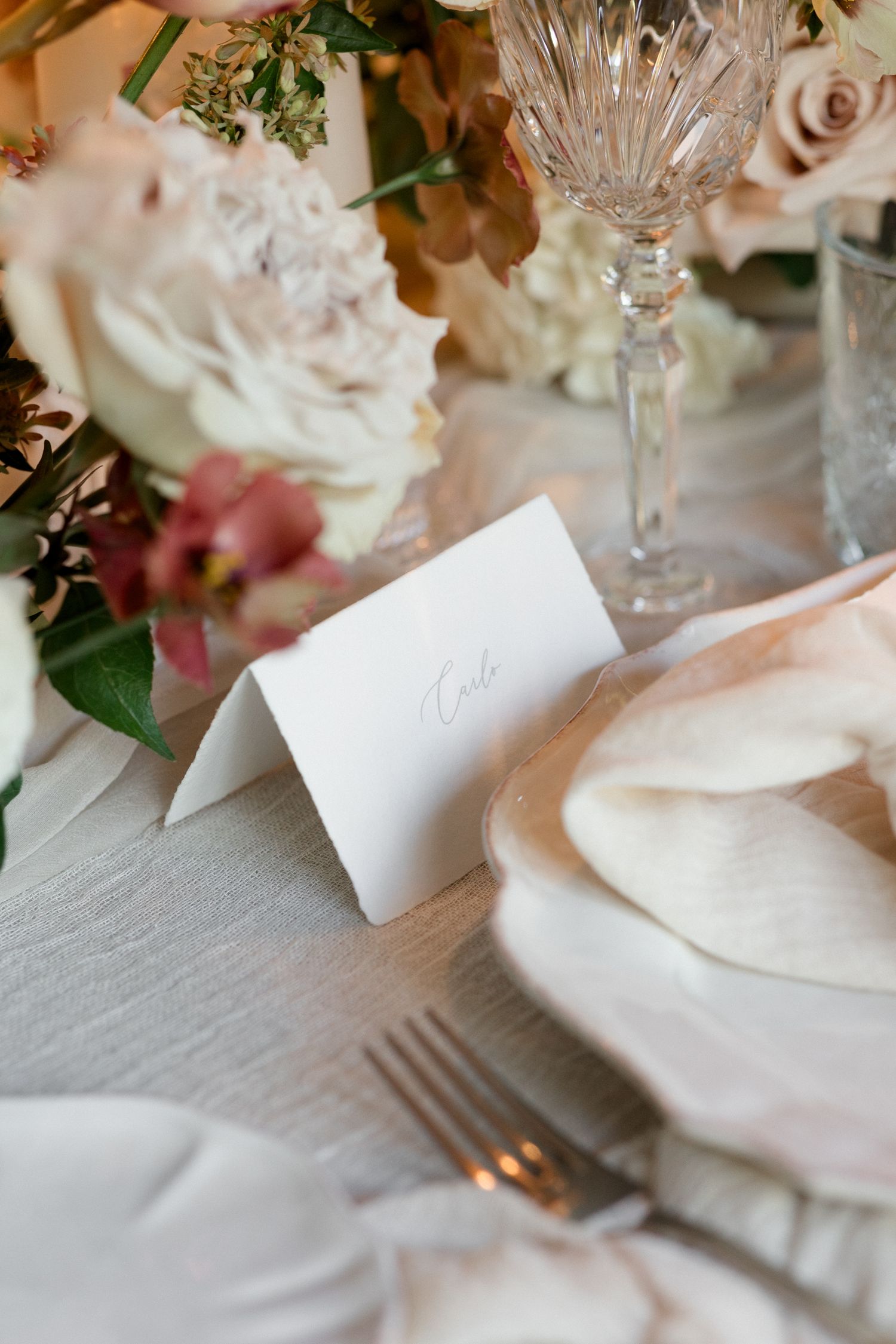 Elegant table setting with crystal glassware, white napkins and soft floral arrangements for a formal dining event.