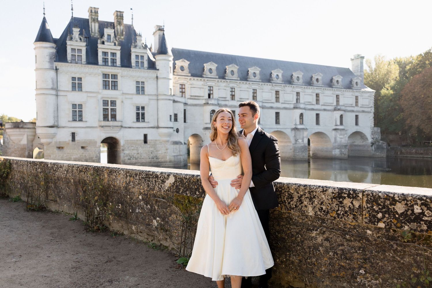 Bride and groom pose on a stone bridge before Château de Chenonceau in the Loire Valley, France.
