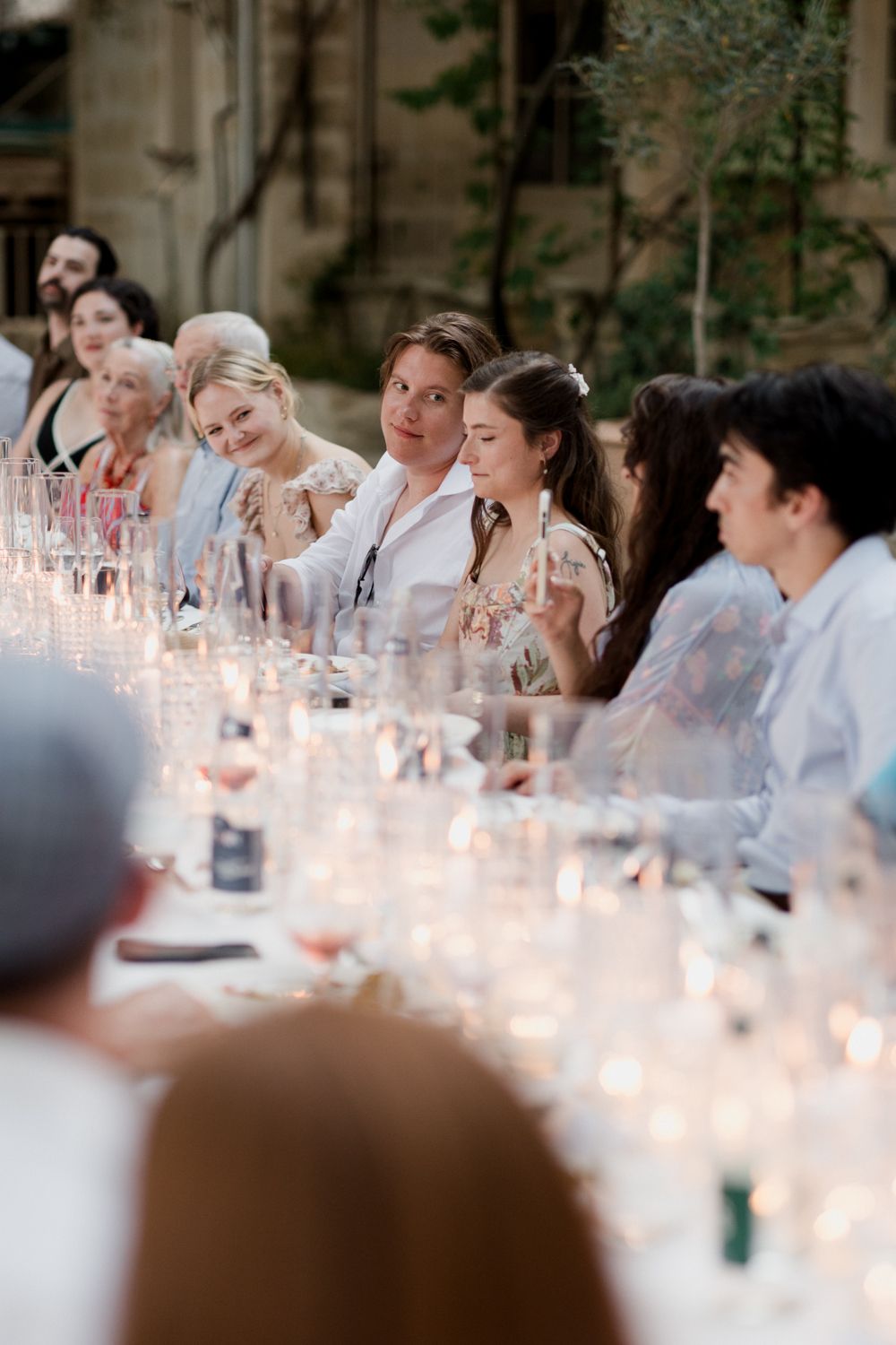 Wedding guests enjoying a candlelit dinner reception with glowing ambiance and glassware on long table. Welcome Event Auberge de la Treille