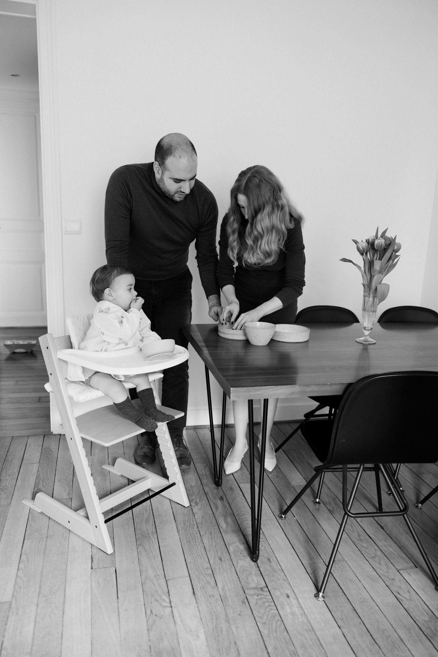 Black and white photo of a family with a baby in a high chair at a dining table in a modern home.