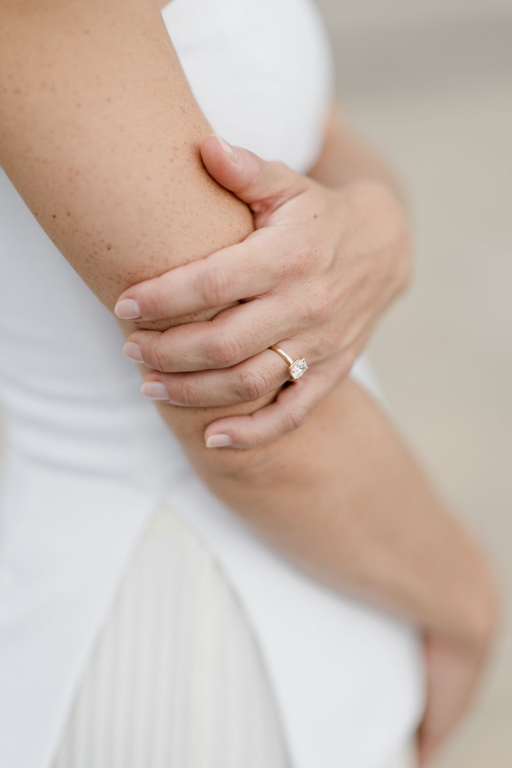 Close-up of hands wearing an engagement ring against white fabric of a wedding dress. Engagement session in Tours
