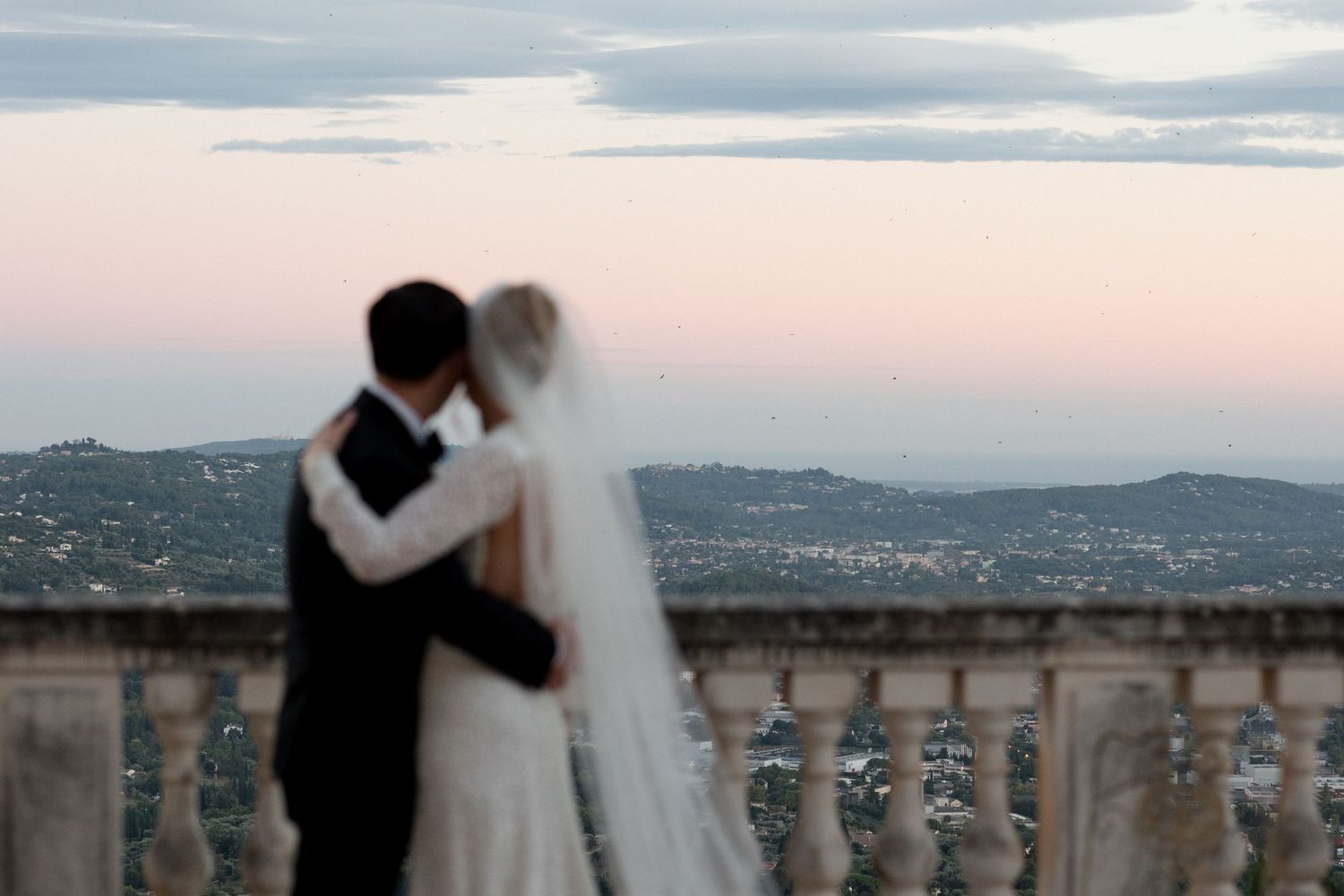 A romantic wedding couple embraces while overlooking a scenic city view at sunset. Mariage Chateau saint georges Grasse France