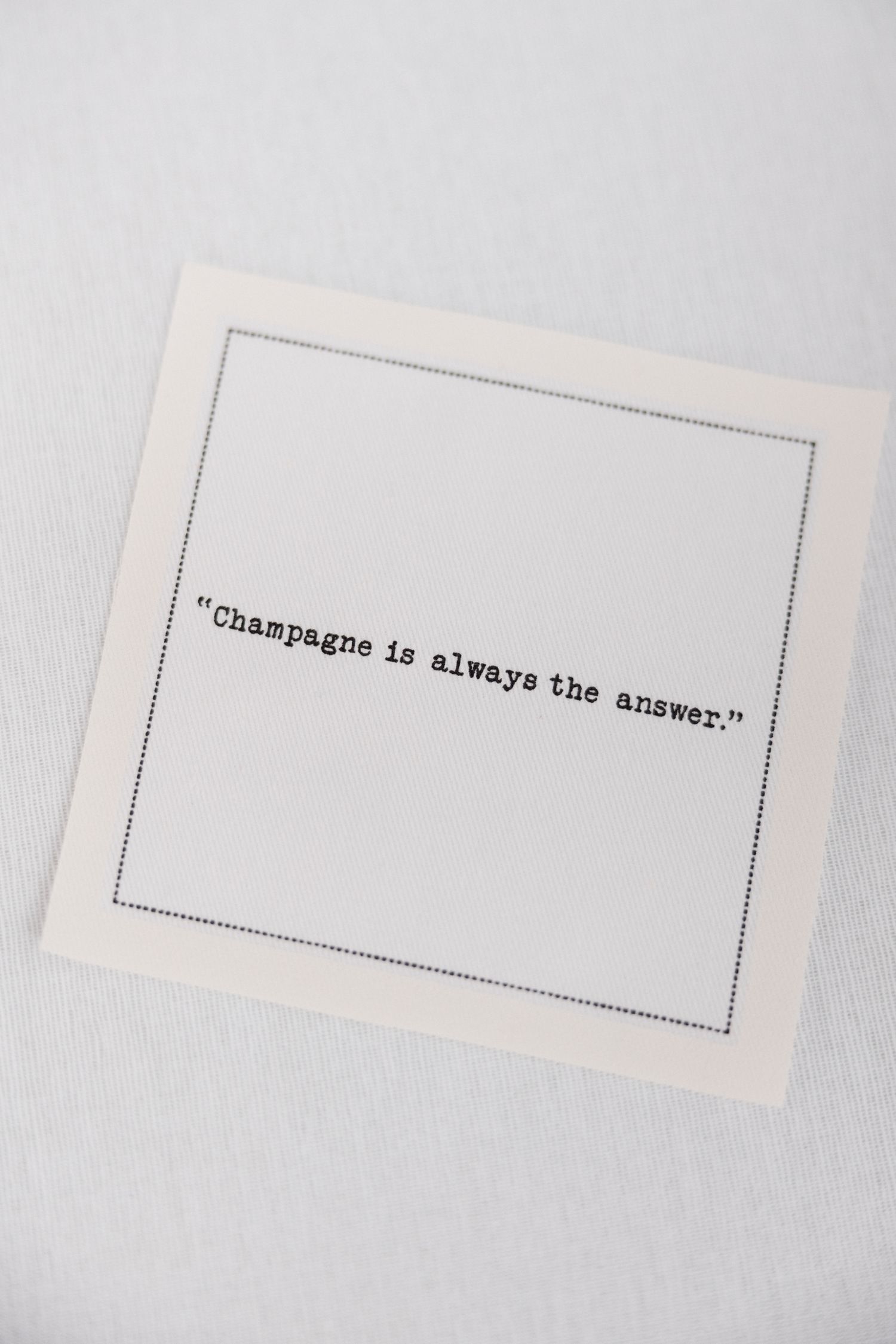 Three minimalist white cards with typewritten text including 'Champagne is always the answer' on a light gray surface.