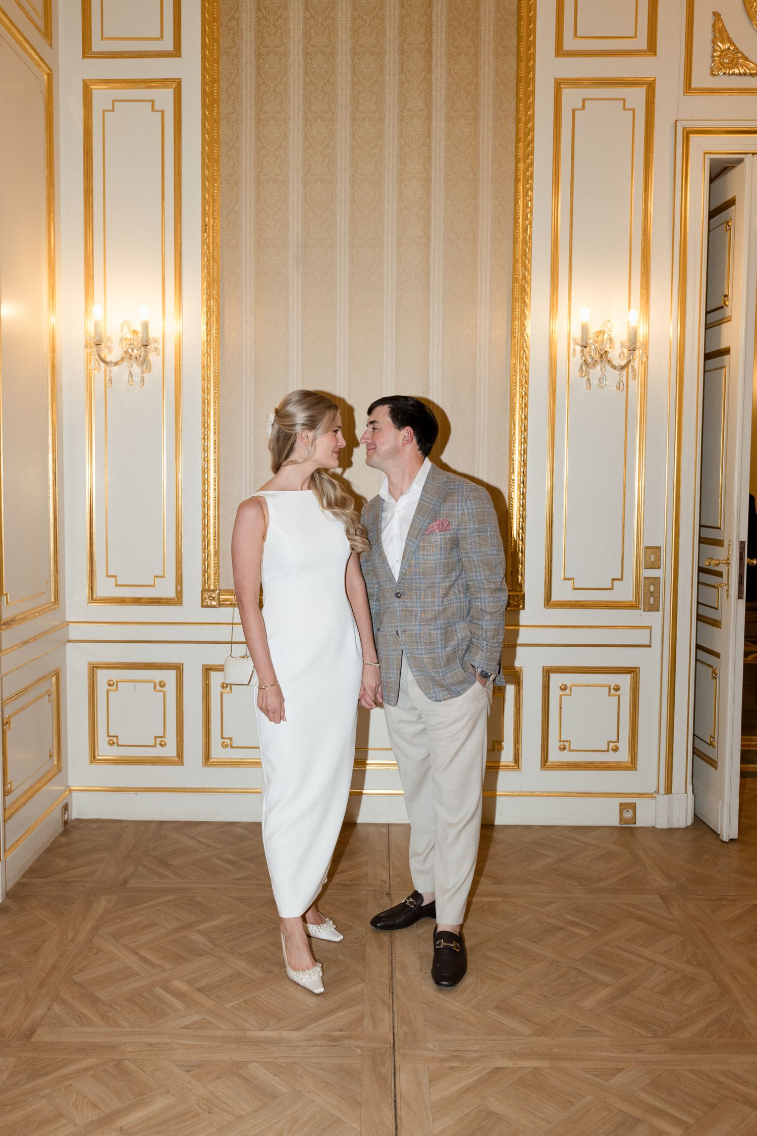 A couple shares a romantic moment in an elegant room with gold-trimmed walls and crystal sconces.