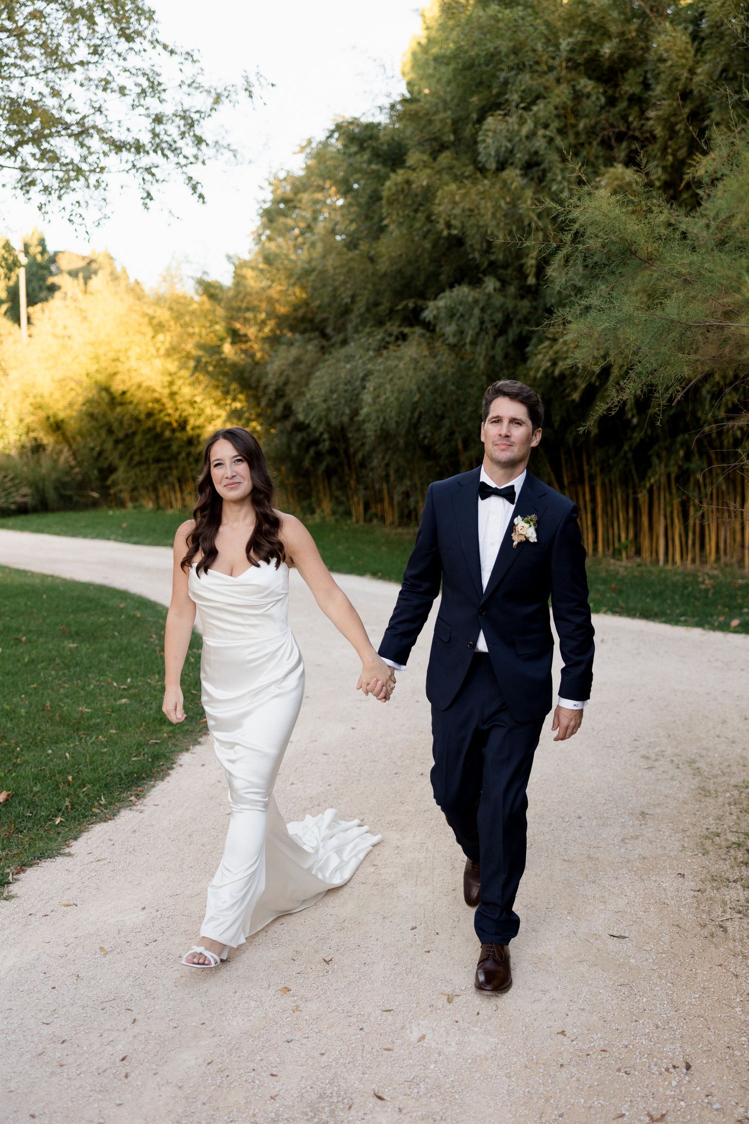 A couple in wedding attire walks and plays together on a dirt path surrounded by trees during golden hour. wedding photographer france