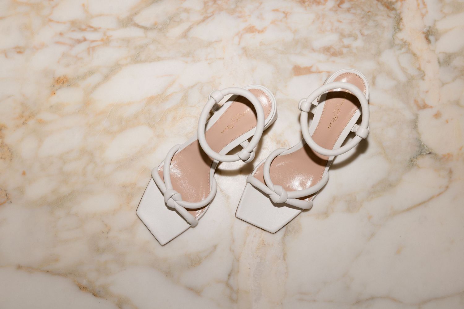 Elegant white leather sandals with metallic buckles displayed on a luxurious marble surface.