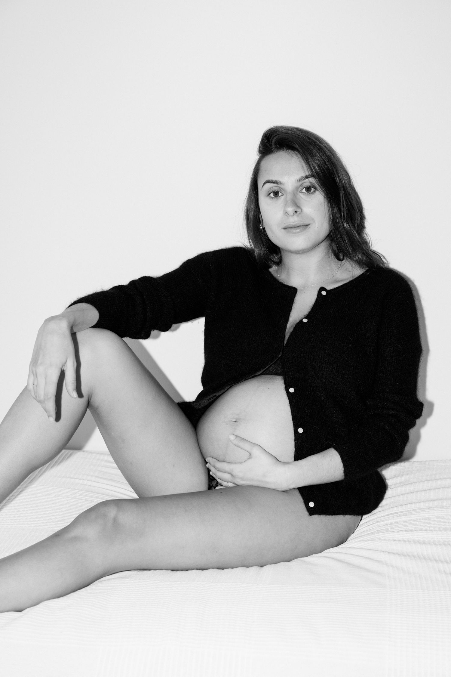 Black and white photo series showing someone in a black shirt reclining on white bedding in various relaxed poses.