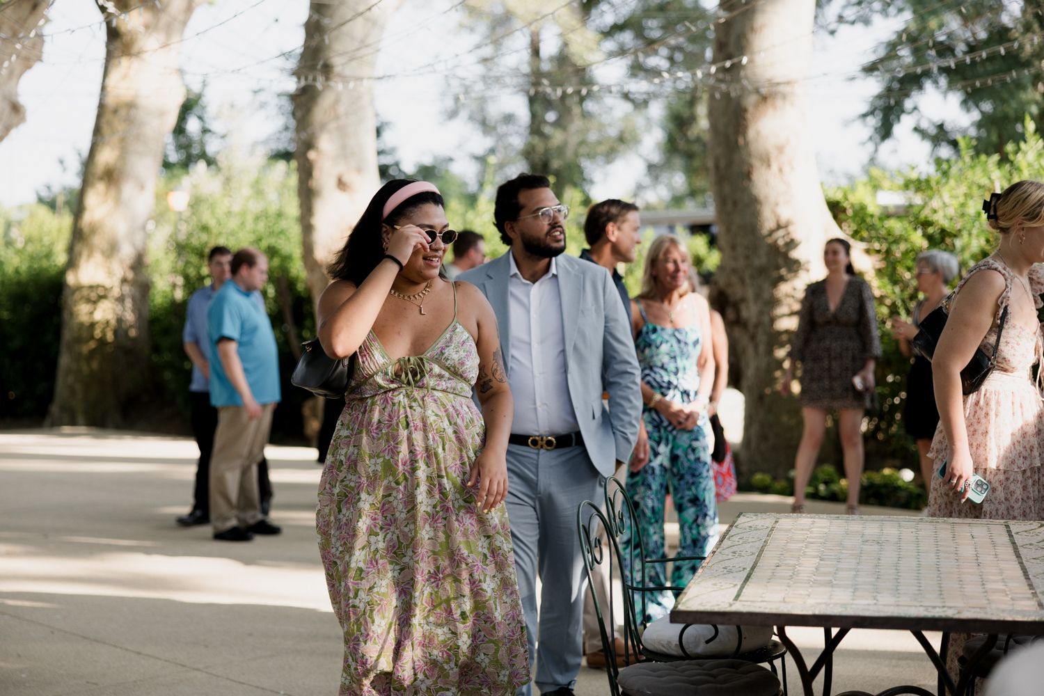 Wedding guests walk along a tree-lined path during an outdoor celebration wearing colorful summer attire.