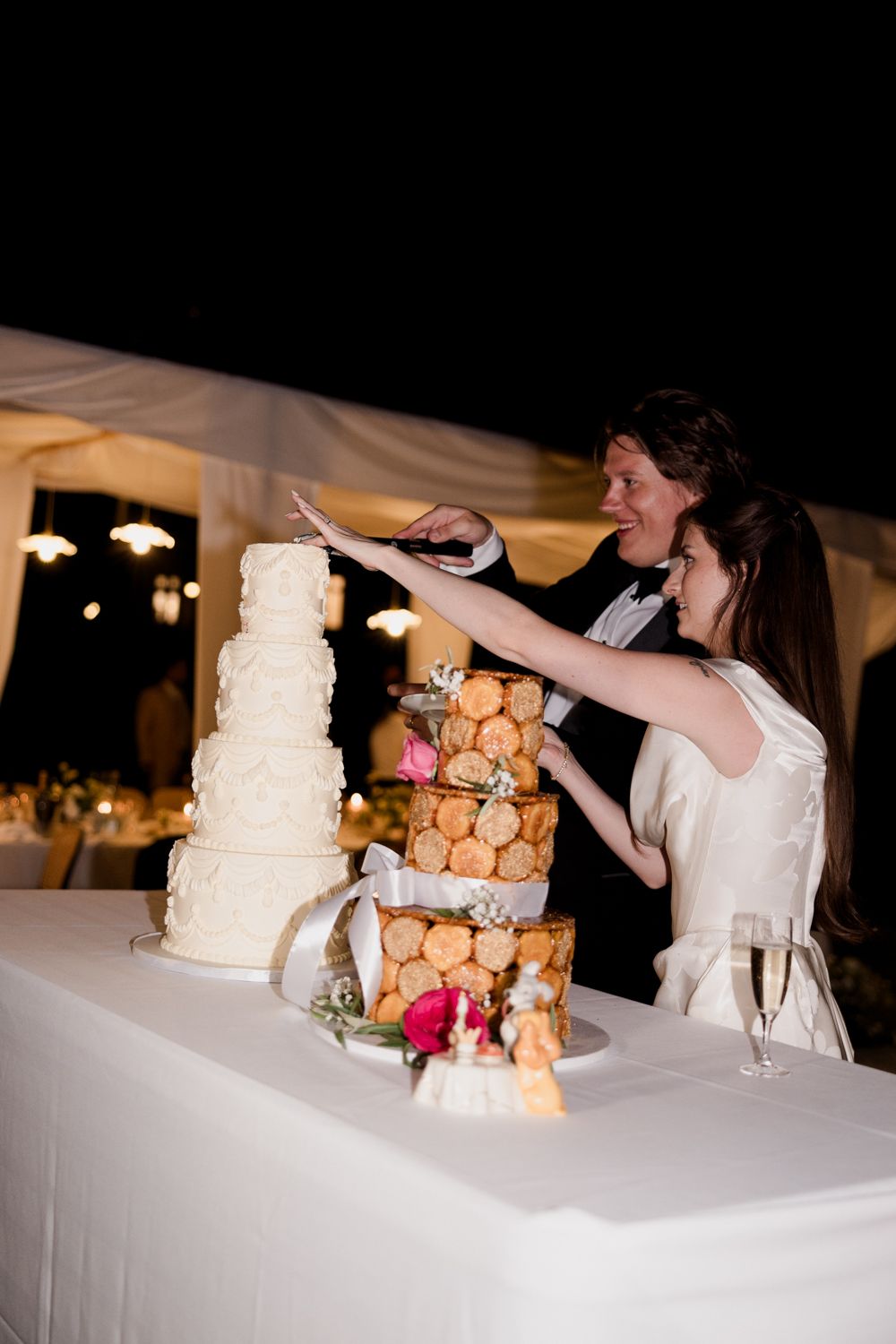 Couple cutting their wedding cake together with a tall white layered cake and cream puffs displayed on a dessert table.