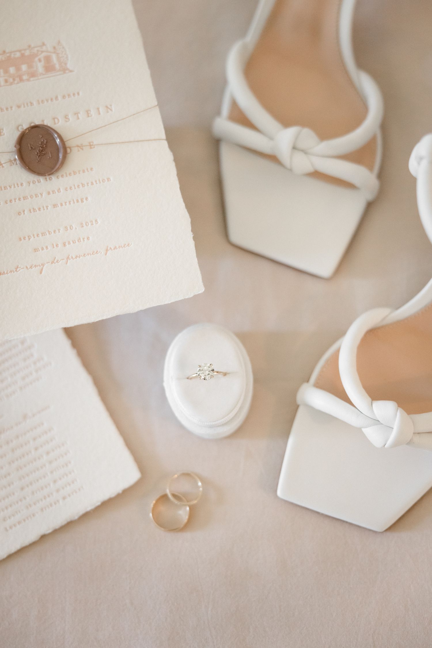Elegant wedding rings and delicate white jewelry boxes arranged on a soft beige textured surface in natural light.