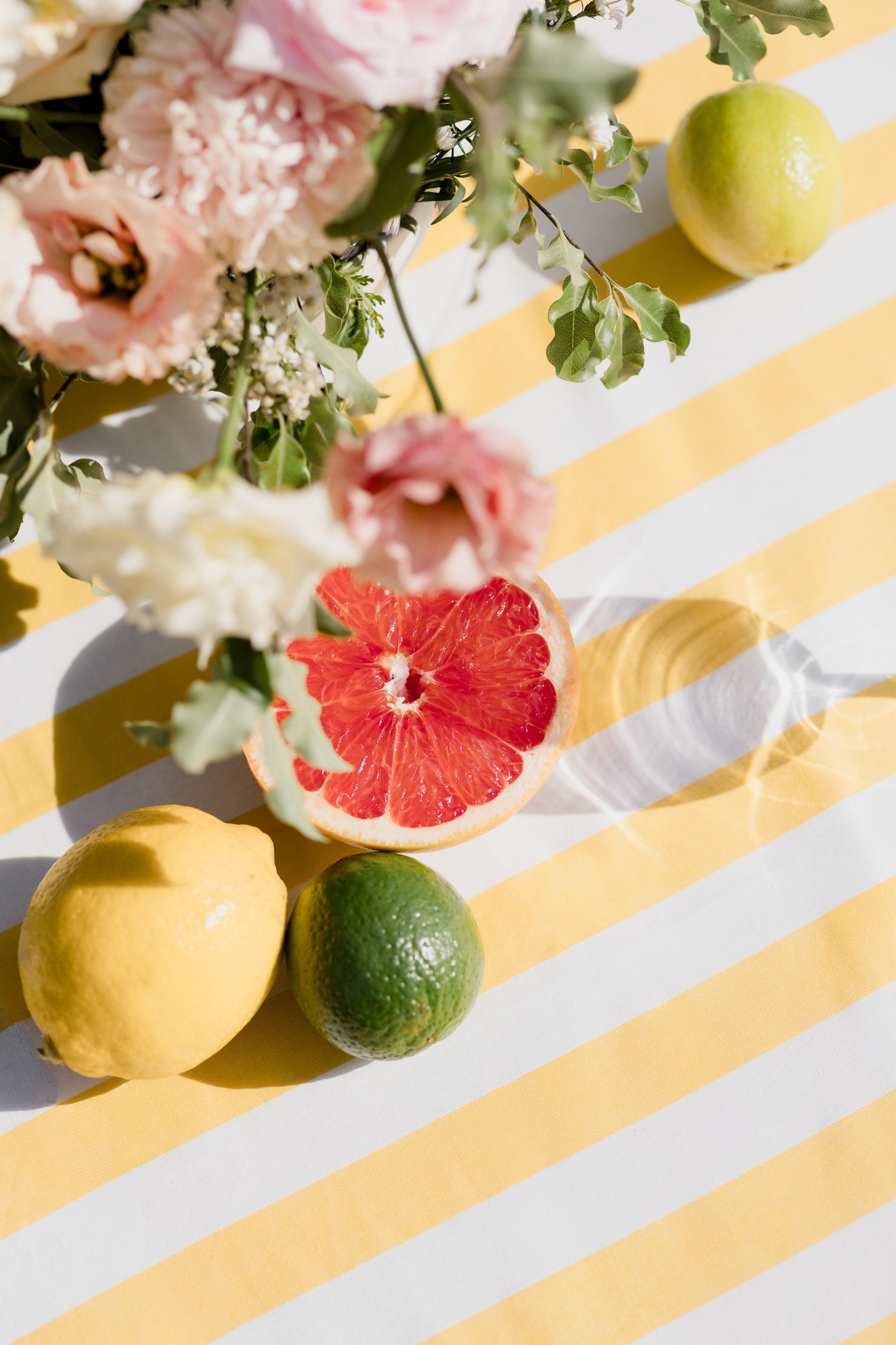 Fresh citrus fruits and pink carnations arranged on a white and yellow striped surface in bright natural lighting. Paris wedding photographe